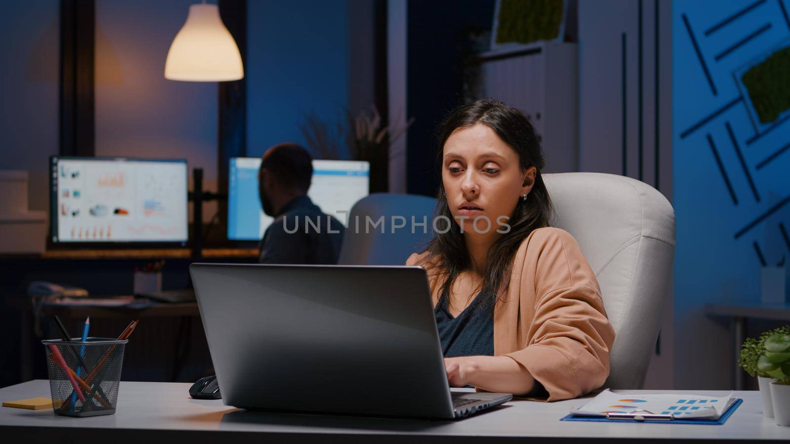 Workaholic entrepreneur woman sitting at desk table analysing financial graphics using laptop computer. Executive businesswoman planning marketing strategy working in startup business company office