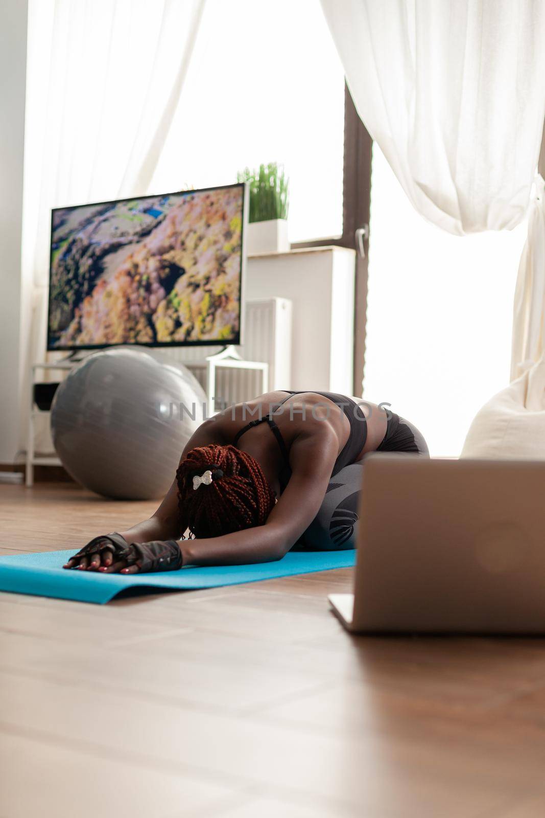 African black fit woman dressed in sportwear relaxing on yoga mat, watching online training exercise using laptop in home living room for wellbeing, Workout and healthy lifestyle.