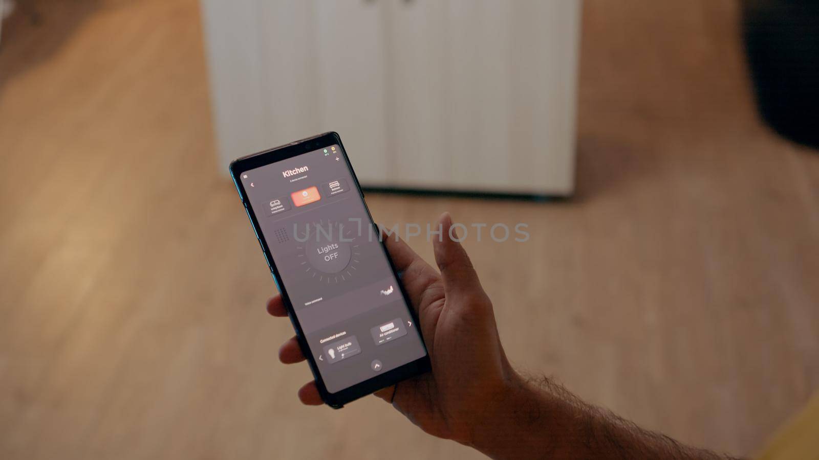 Close up of man using voice activated application to turn on bulbs in smart home with automation system. Person holding phone with modern software controlling lights in house before start working