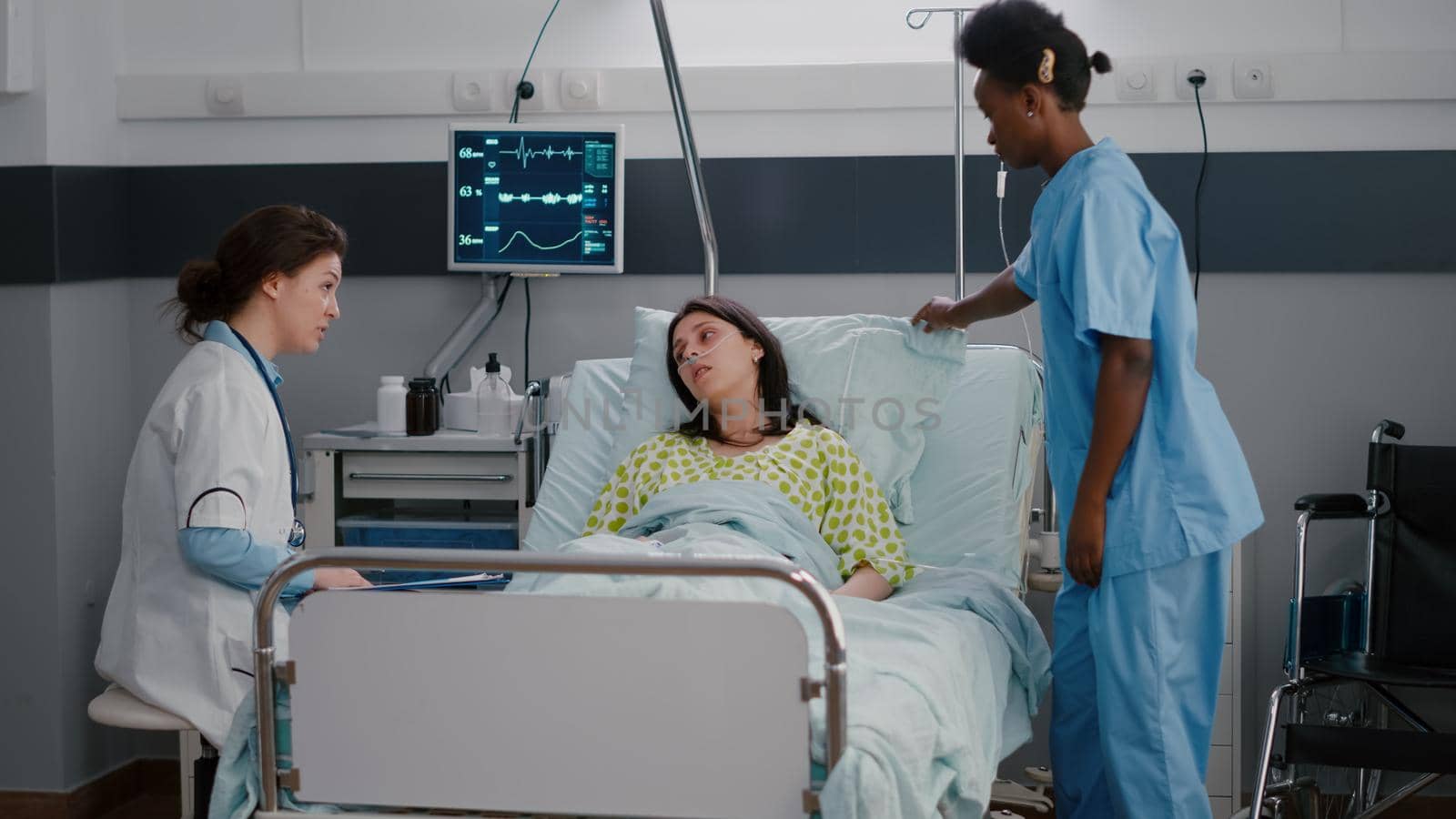 Nurse with dark skin helping patient to sit comfortable in hospital ward by DCStudio