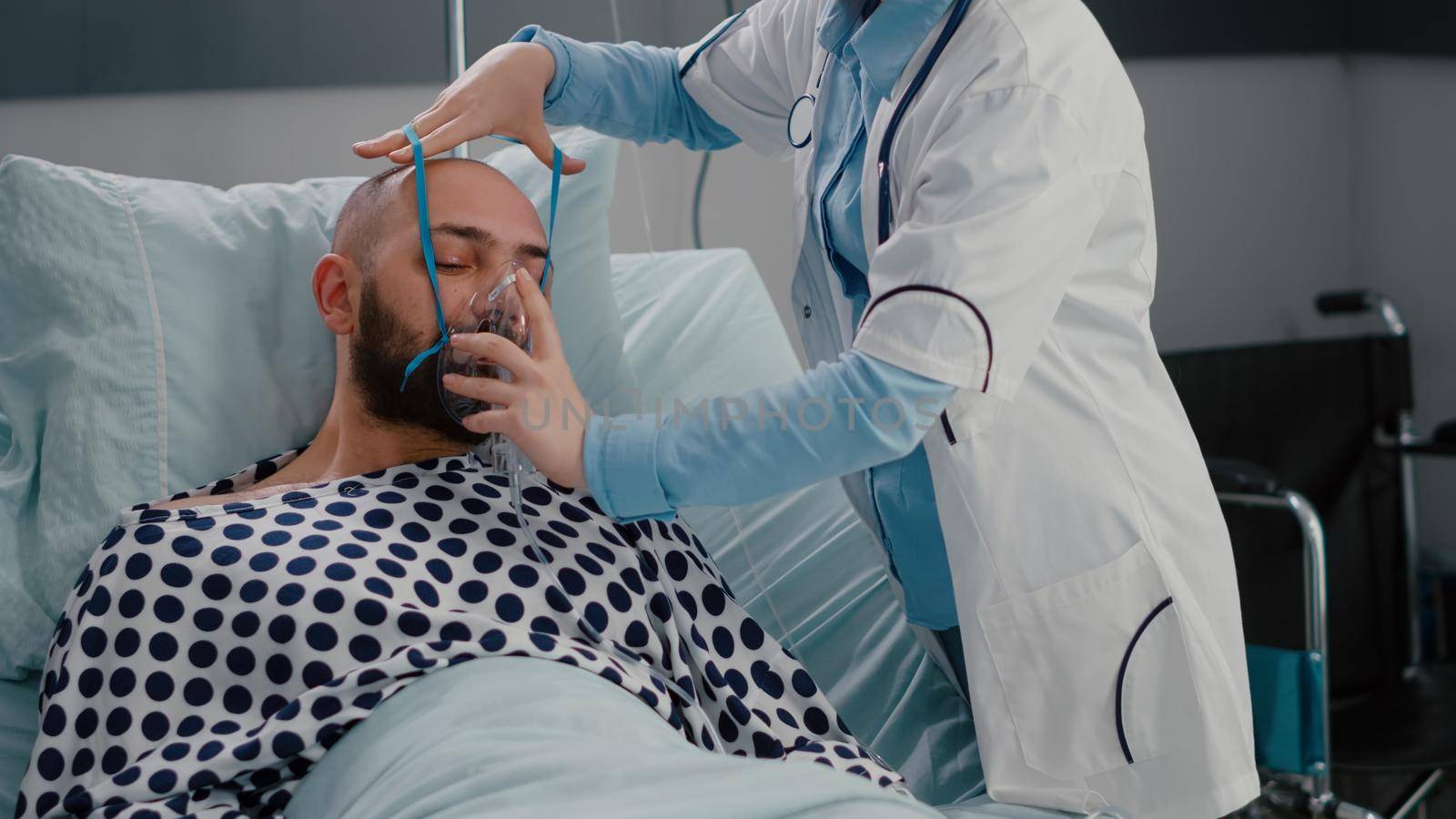 Patient sitting in bed while woman doctor putting oxygen mask by DCStudio