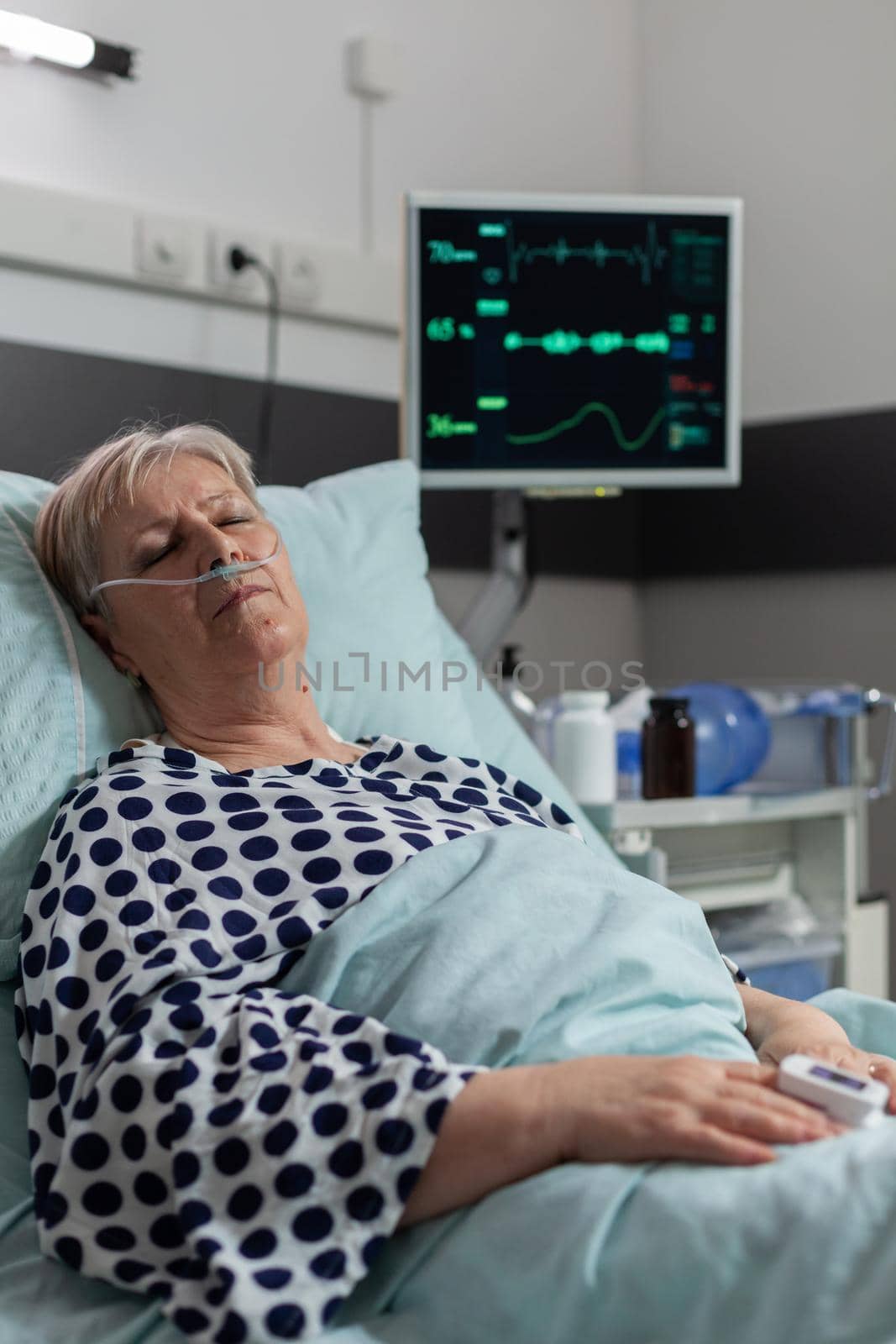 Senior woman patient laying in hospital bed with oxymeter attached on body, measuring oxygen saturation from blood and blood pressure and bmp. Getting treatment from iv drip bag.