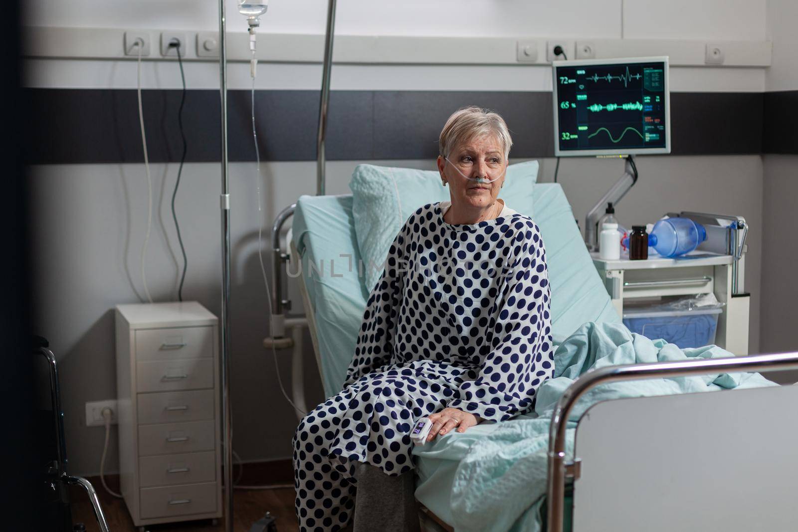 Senior woman patient sitting on the edge of bed in hospital bed by DCStudio