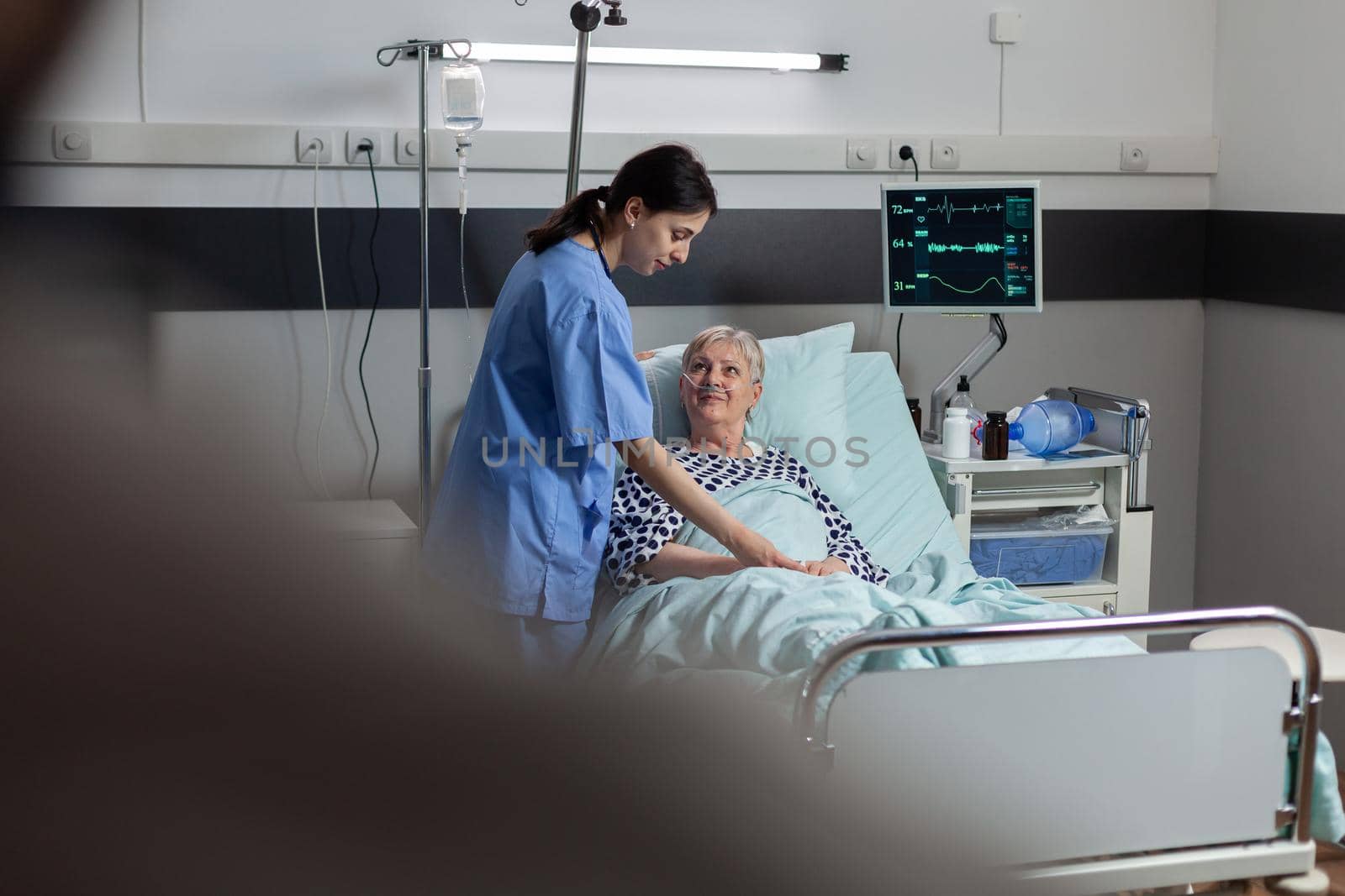 Fiendly doctor hands holding patient hand, in hospital room giving encouragement, empathy, support during medical examination. Patient breathing through oxygen mask.