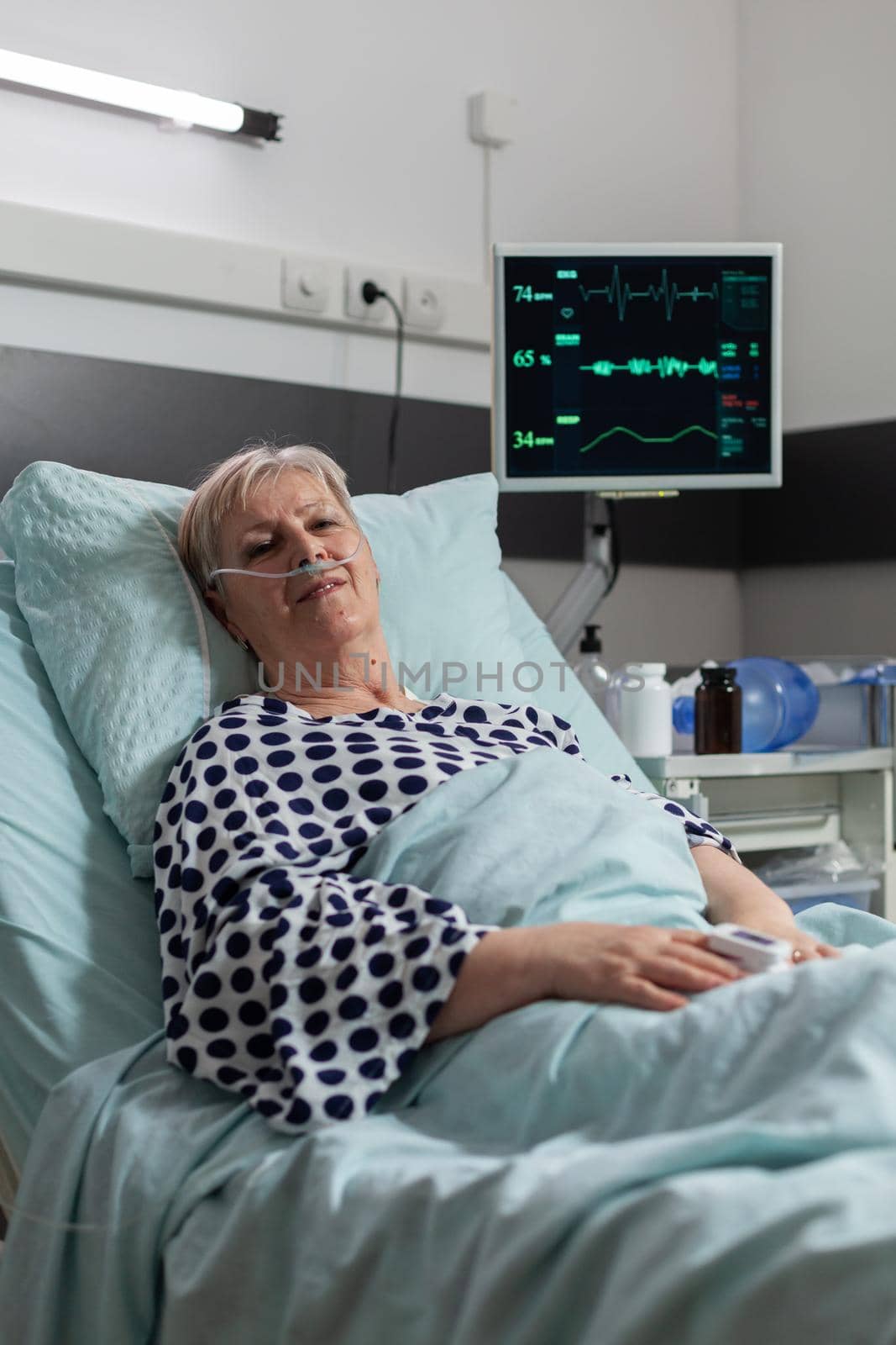 Senior elderly person with pulmonary failure breathing with help from oxygen mask, laying in hospital bed, getting treatment through iv drip bag. Patient bmp on monitor.