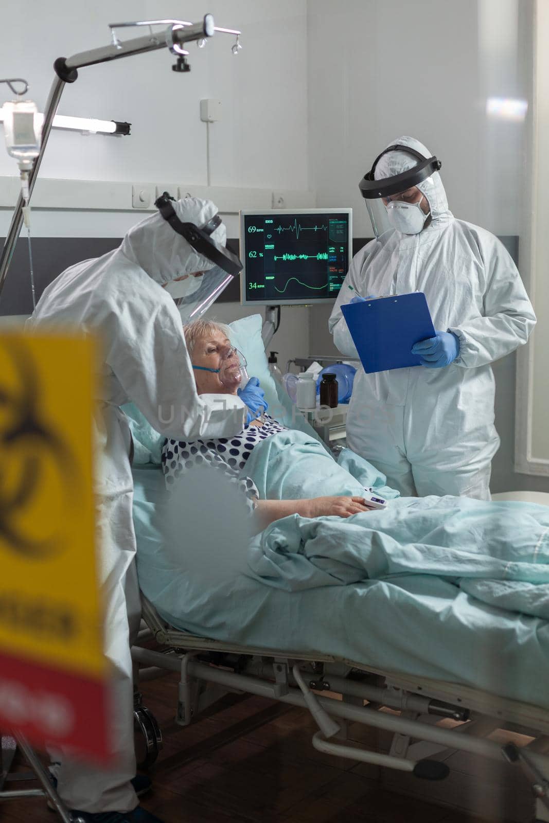 Medical nurse dressed in ppe suit putting oxygen mask to senior patient by DCStudio