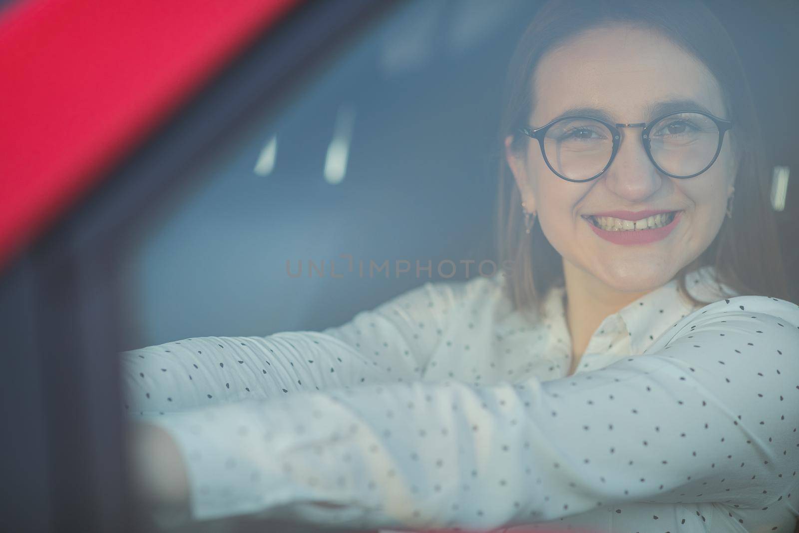 Beautiful attractive woman in car, looking through the window and smile. Portrait of Caucasian woman looking through car window to the camera and smiling