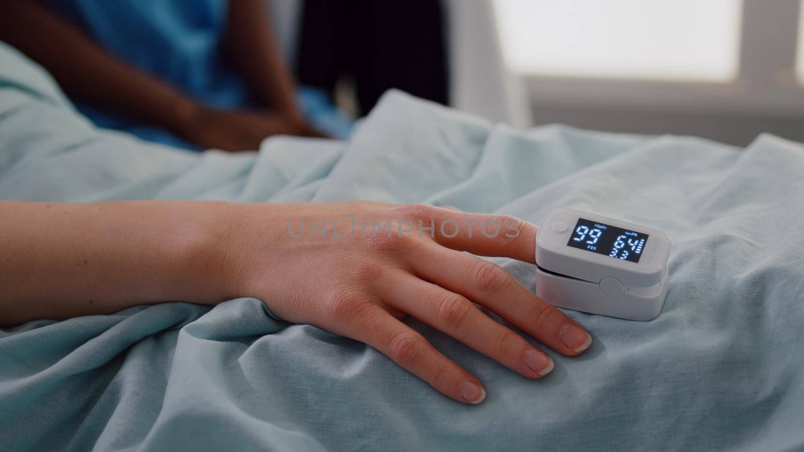 Close up of hospitalized woman with finger heart rate monitor showing pulse while resting in bed during cardiology consultation in hospital ward. Patient with oximeter waiting for sickness treatment