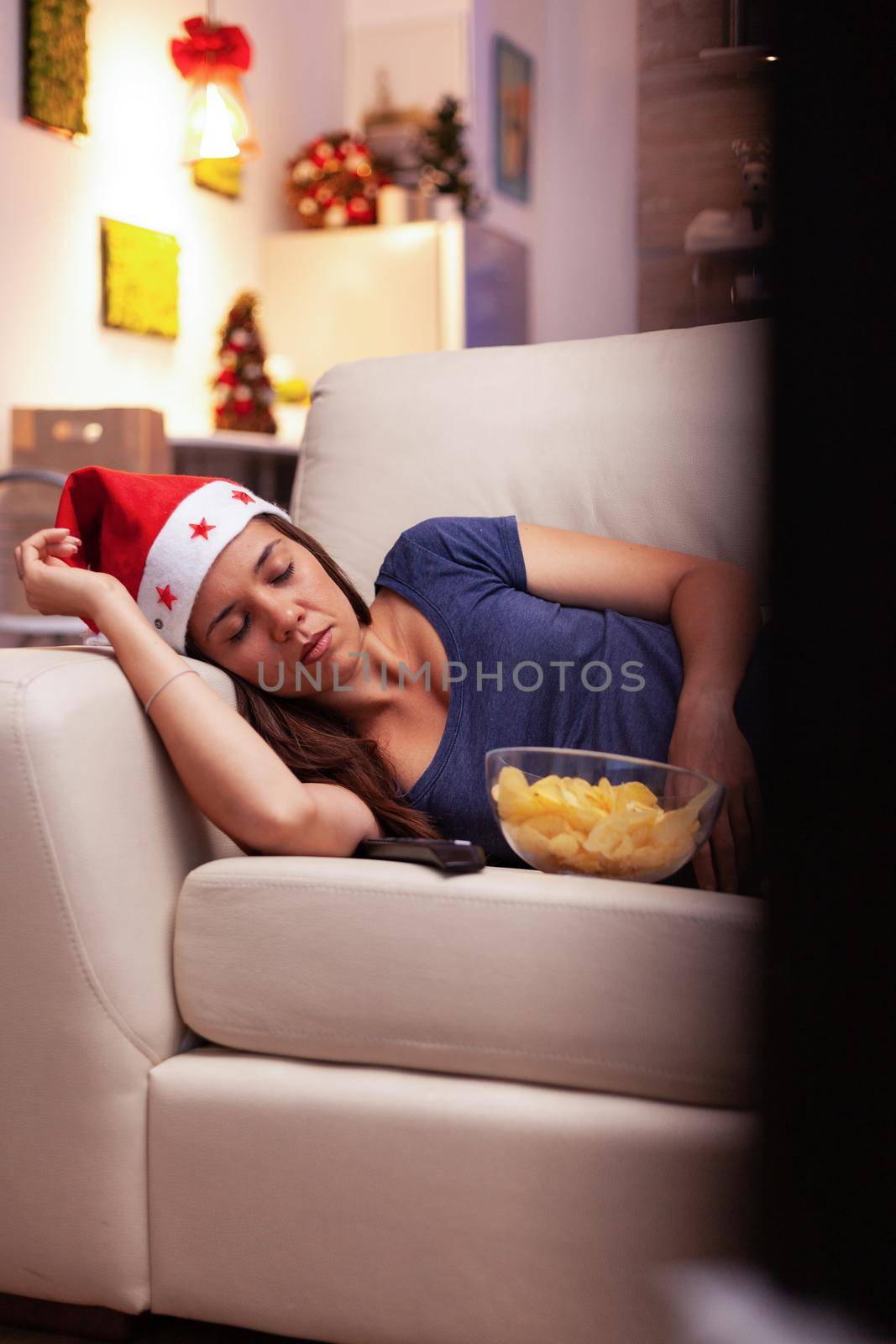 Woman sleeping on couch after watching xmas comedy movie on television in x-mas decorated kitchen. Girl enjoying winter season celebrating christmas holiday alone at home
