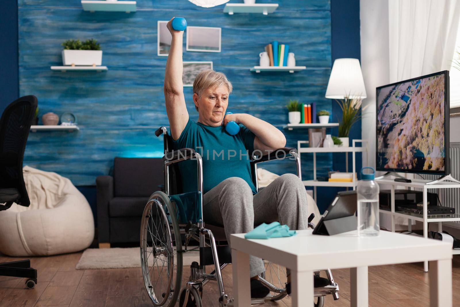 Disabled old woman in wheelchair raising arm training muscles resistance using dumbbells by DCStudio