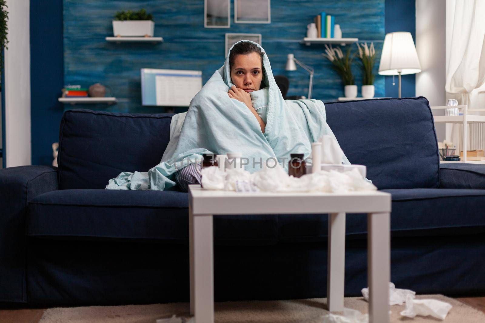 Sick woman wrapped in blanket on sofa at home by DCStudio