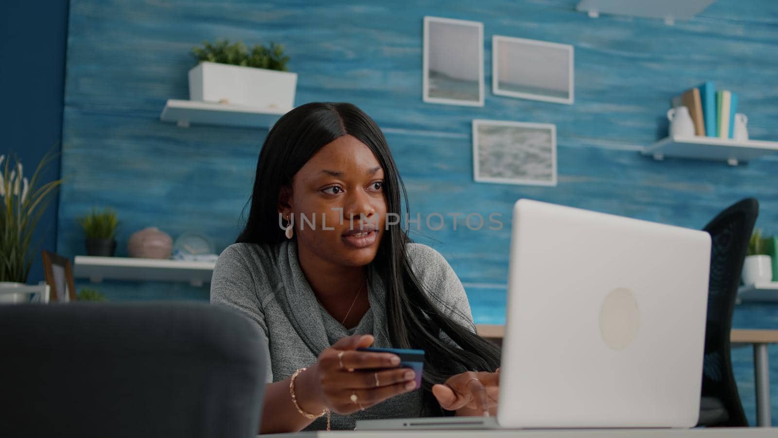 African american student holding cred card in hands doing online shopping searching store, easy payment using digital gadget. Black woman browsing internet banking service on laptop in living room