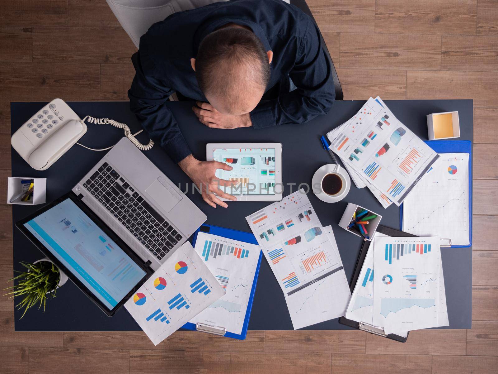 Top view of businessman using tablet pc analyzing financial charts and documents, sitting at desk in corporate office. Employee scrolling through graphs. Successful entrepreneur analyzing strategy.