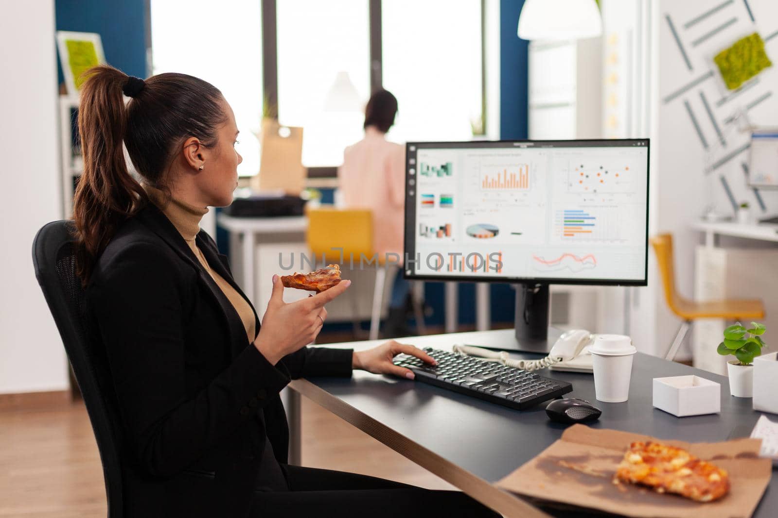 Businesswoman having delivery food order on desk during takeout lunchtime working in business company office. Entrepreneur woman eating takeaway lunch pizza slice management statistics.