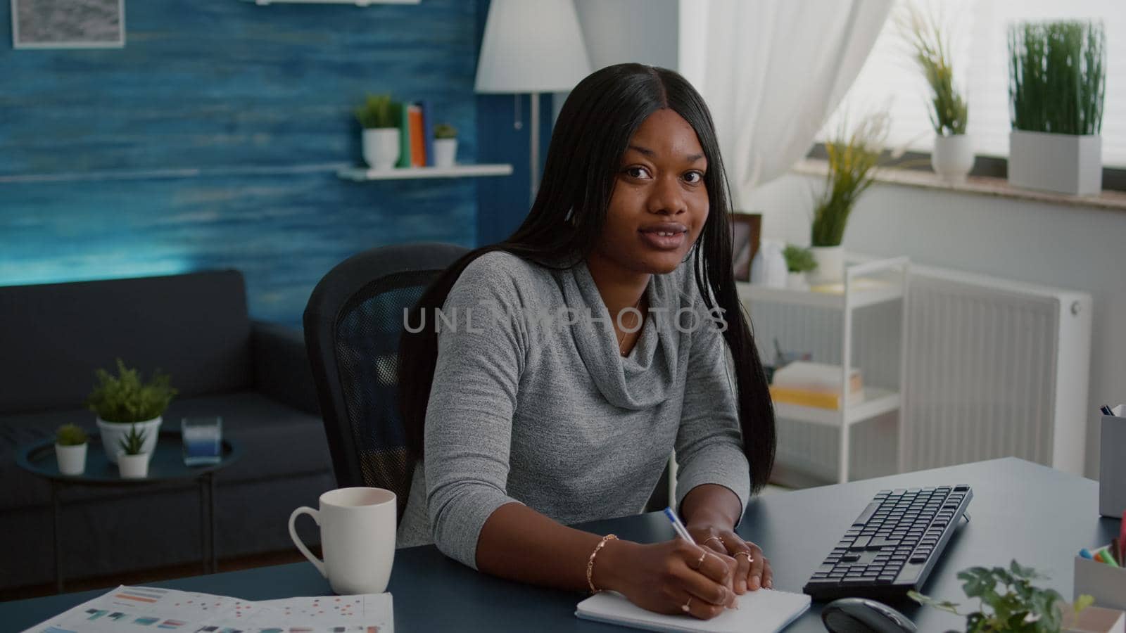 Student with black skin browsing online courses writing school homework on notebook during online webinar education. Young woman sitting at desk table in living room typing lifestyle information