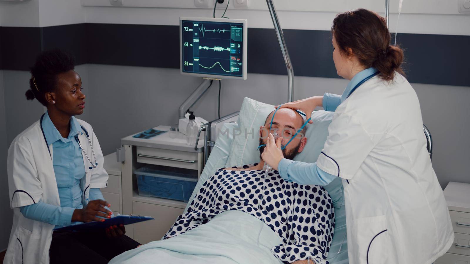 Medical team monitoring heartbeat of sick man during respiratory appointment working in hospital ward. Patient resting in bed while doctor putting oxygen mask checking breath condition