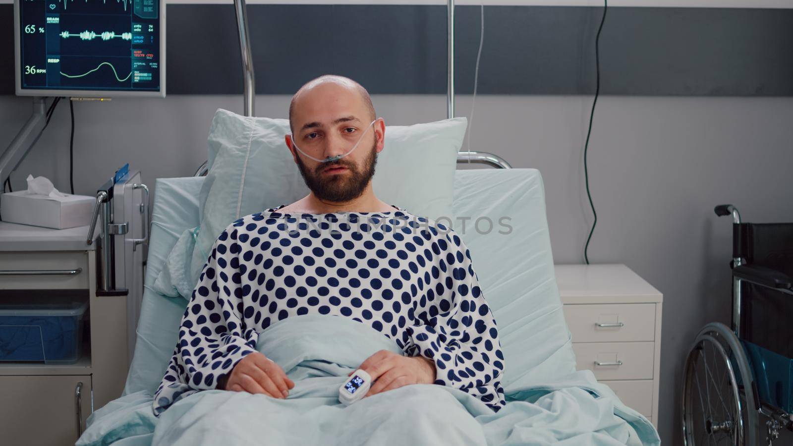 Potrait of sick man wearing nasal oxygen tube having respiratory disease lying in bed during recovering treatment. Patient waiting for physician while looking at camera in hospital ward