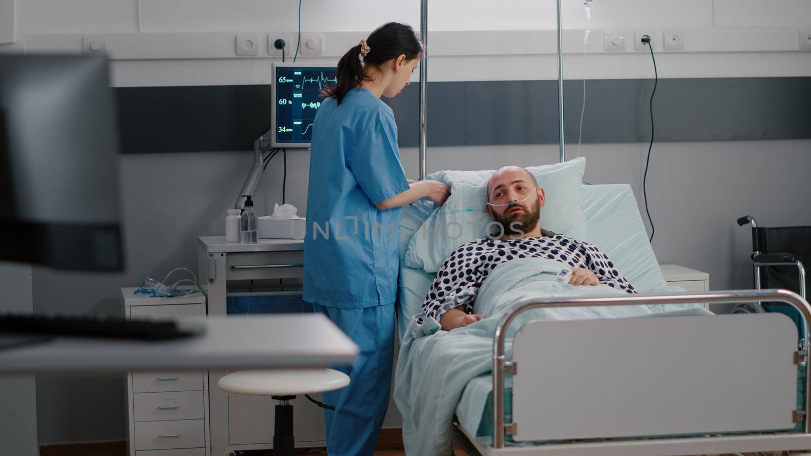 Practitioner asisstant arrange patient bed to sick man during sickness recovery monitoring disease symptom working in hospital ward. Hospitalized patient having respiratory disorder