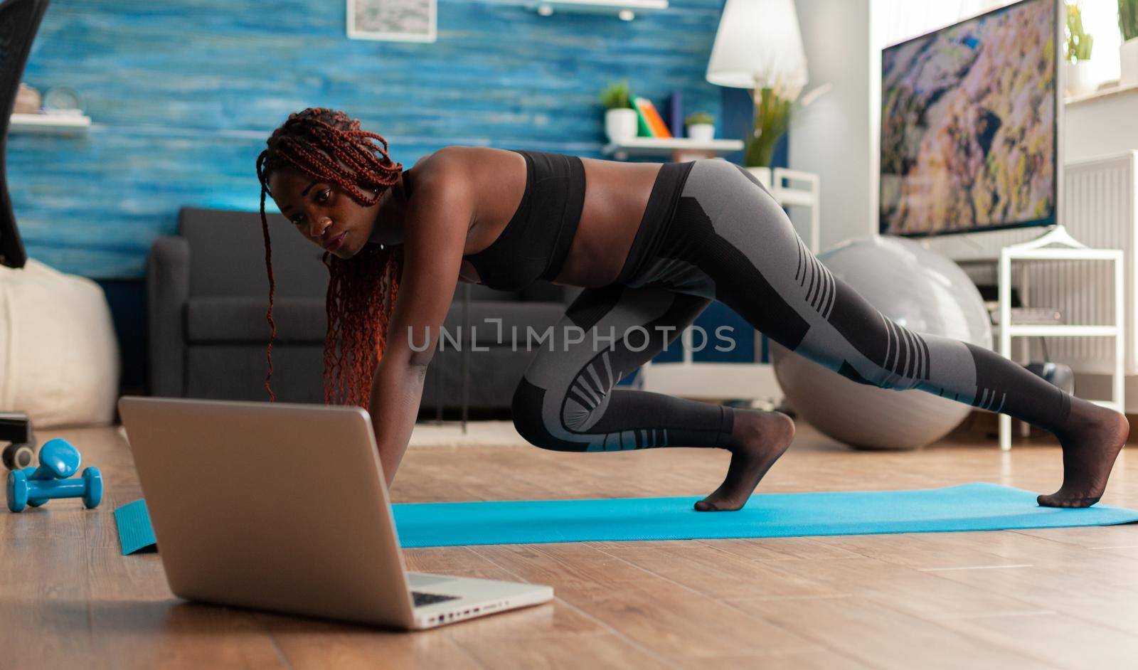 Fit strong black woman doing running plank on fitness mat on living room floor, practicing muntaing climbers workout style for healthy lifestyle wearing leggings and black top.