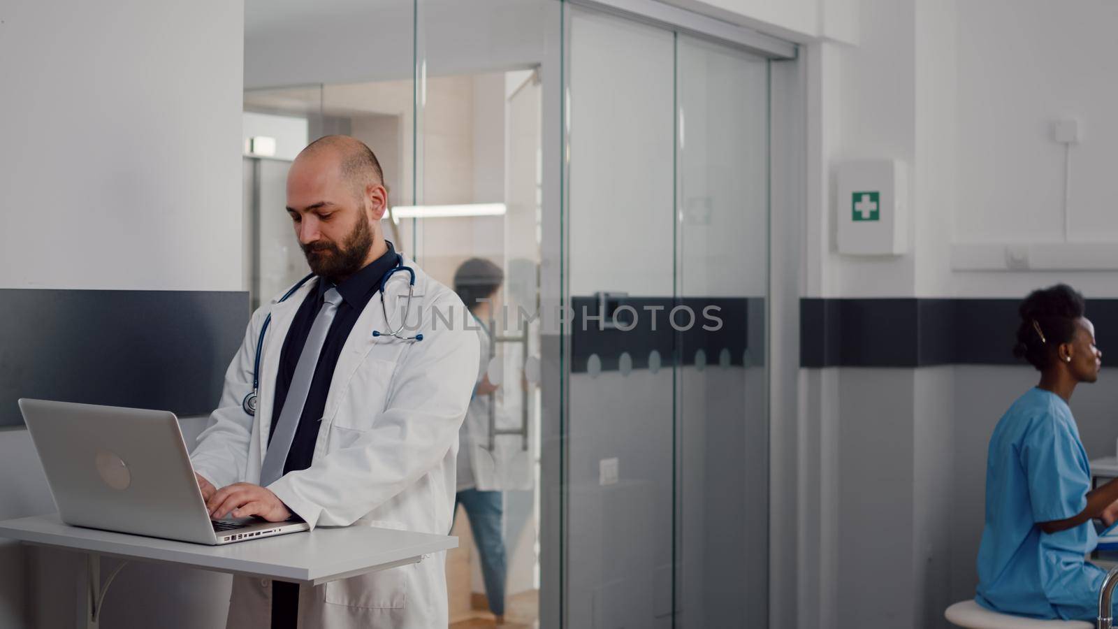 Close up of surgeon doctor wearing medical uniform typing recovery treatment on laptop for sick woman in hospital ward. Black asisstant with hospitalized patient after surgery getting health care