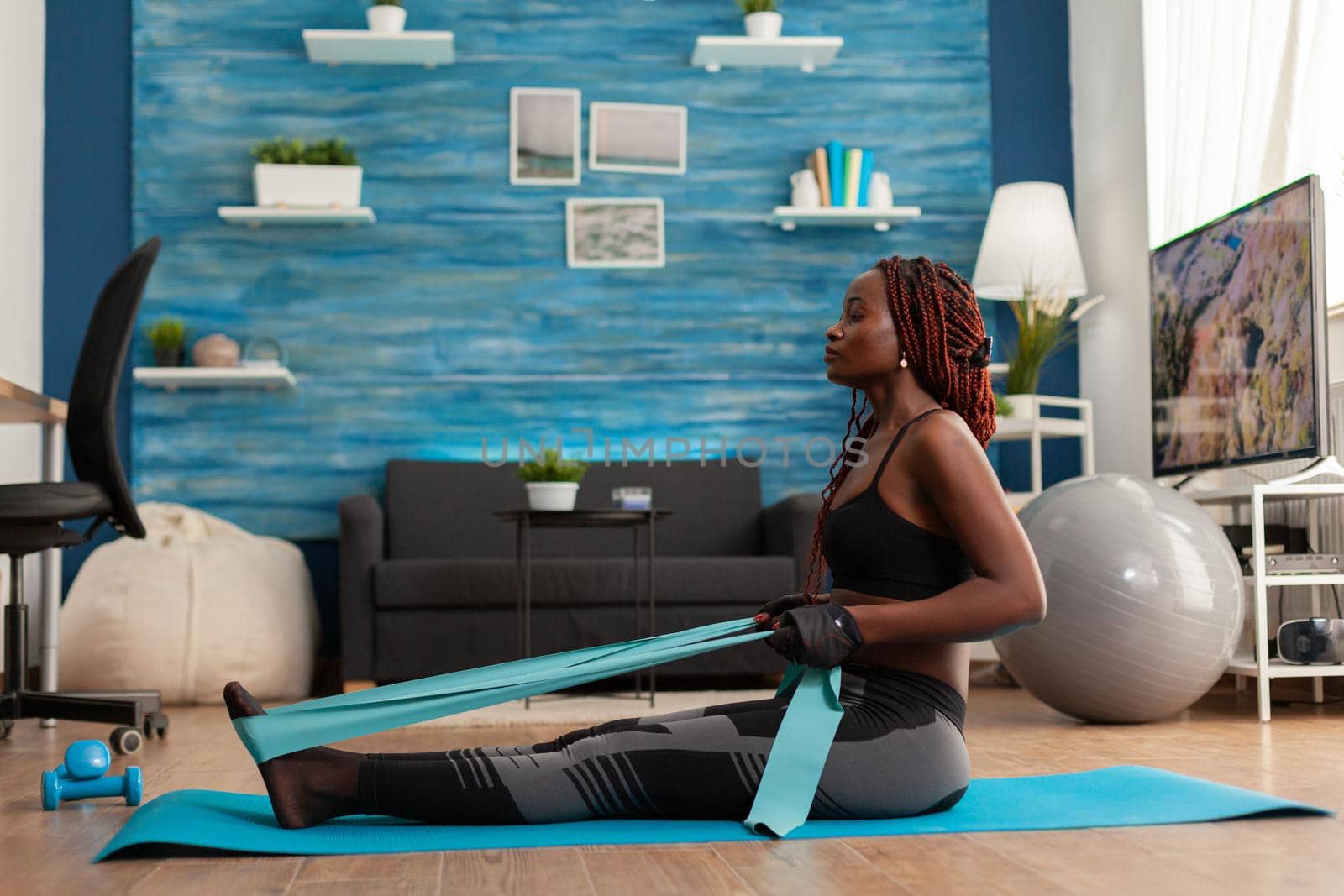 Fit strong afro woman training home living room using resistance band by DCStudio