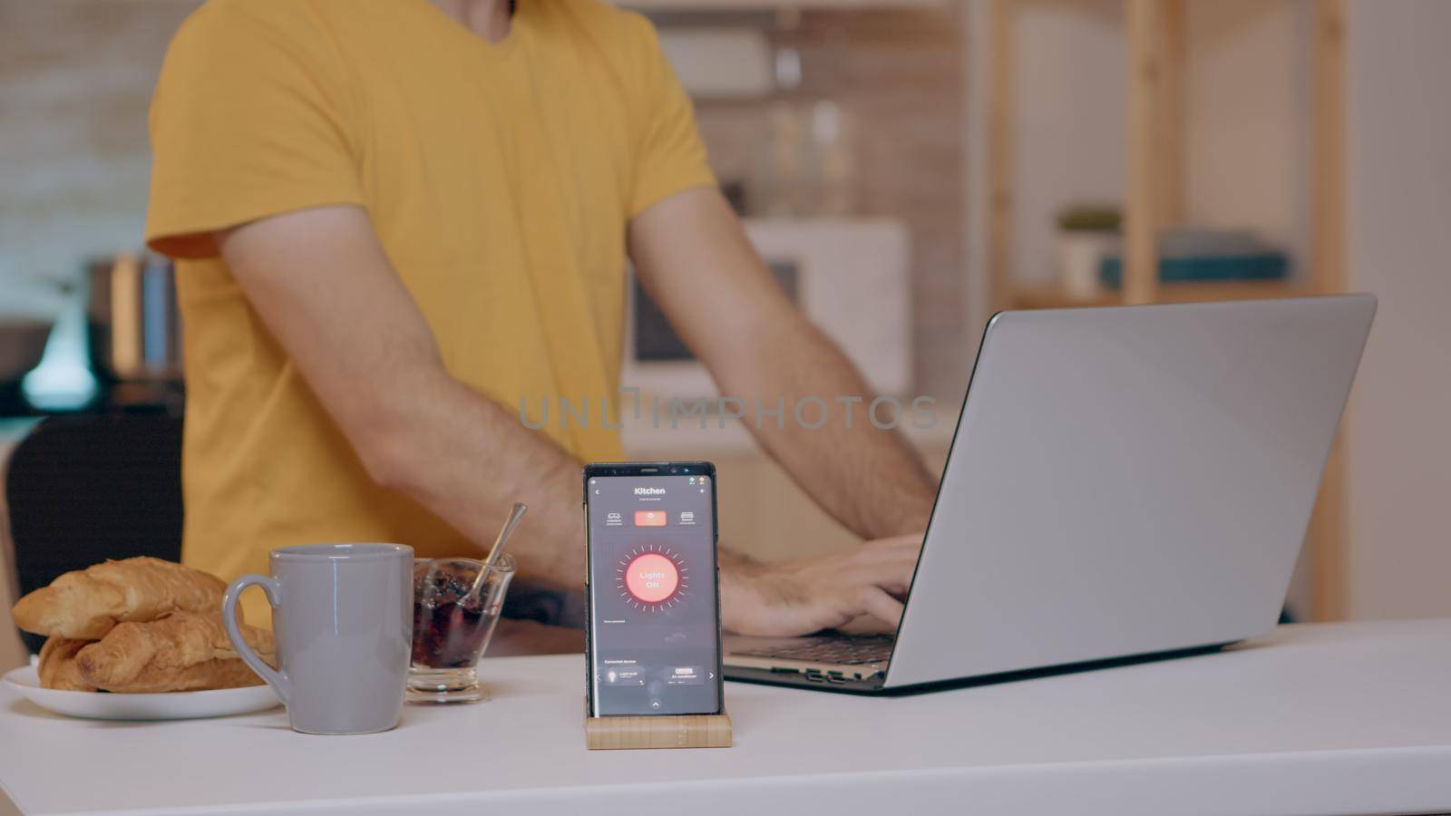 Man working from home with automation lighting system using voice controlled on smartphone turning on the light. Smart speaker gadget responds to commands, person controlling electricity effiency
