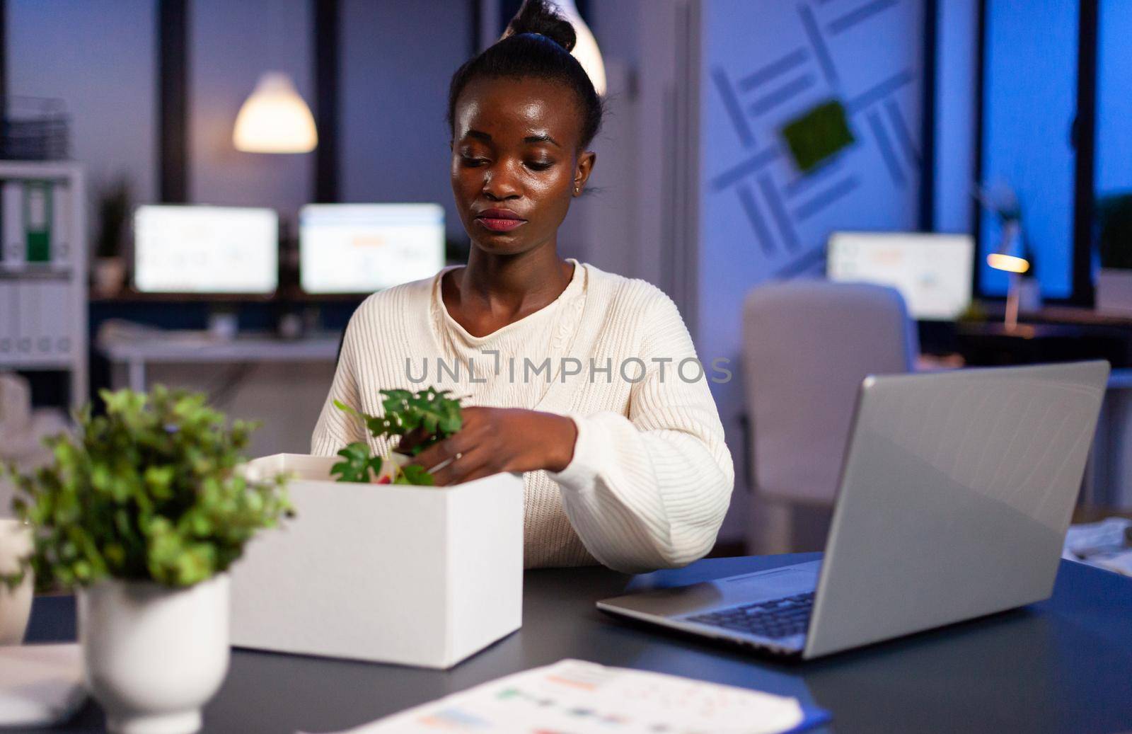 Sad african woman being fired during economy collapse, depressed, unhappy. Unemployed packing things late at night. woman leaving workplace office in midnight.