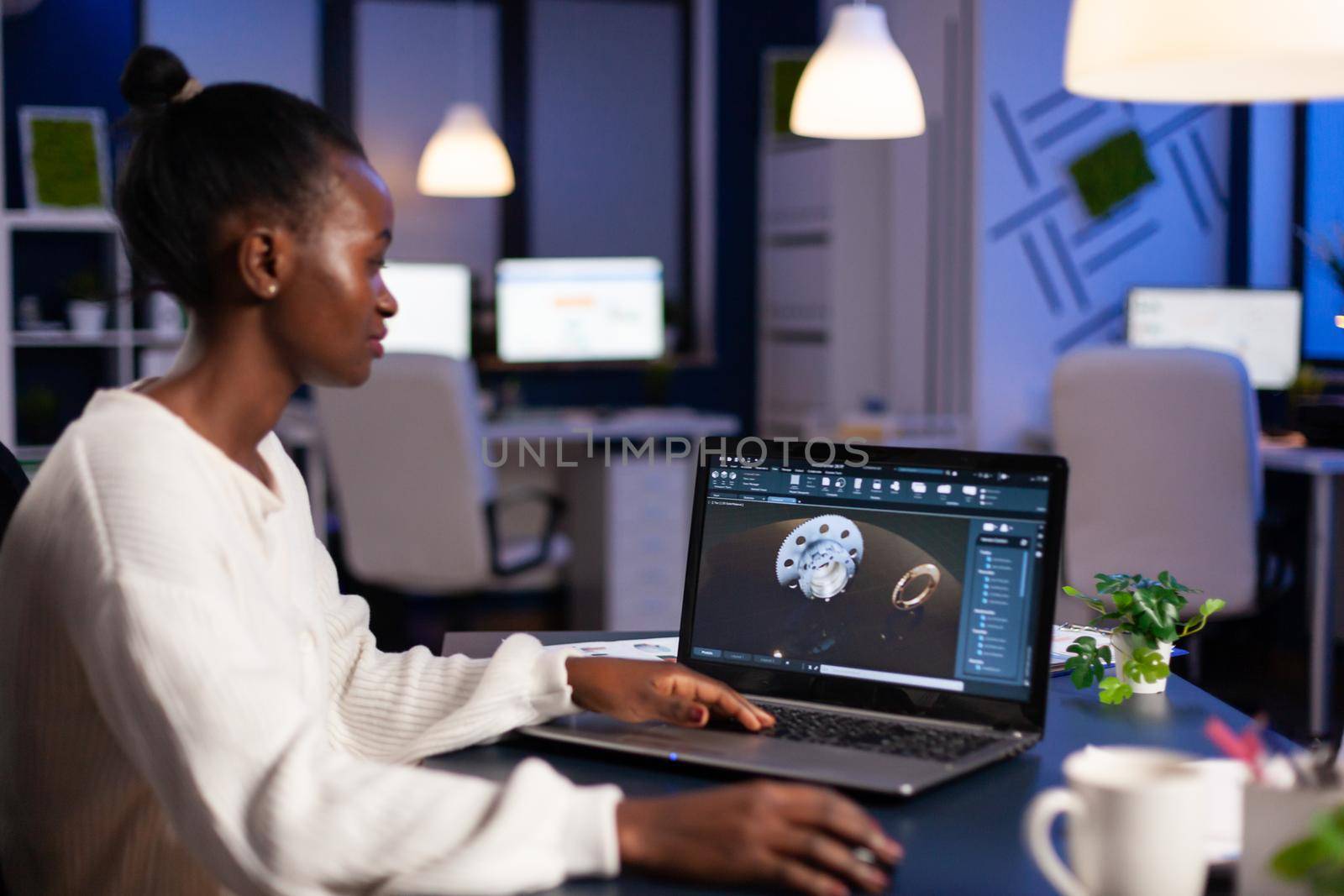 Black woman in mechanical industry working late at night doing overtime in start-up office. Industrial engineer studying prototype idea on pc showing cad software on device display.