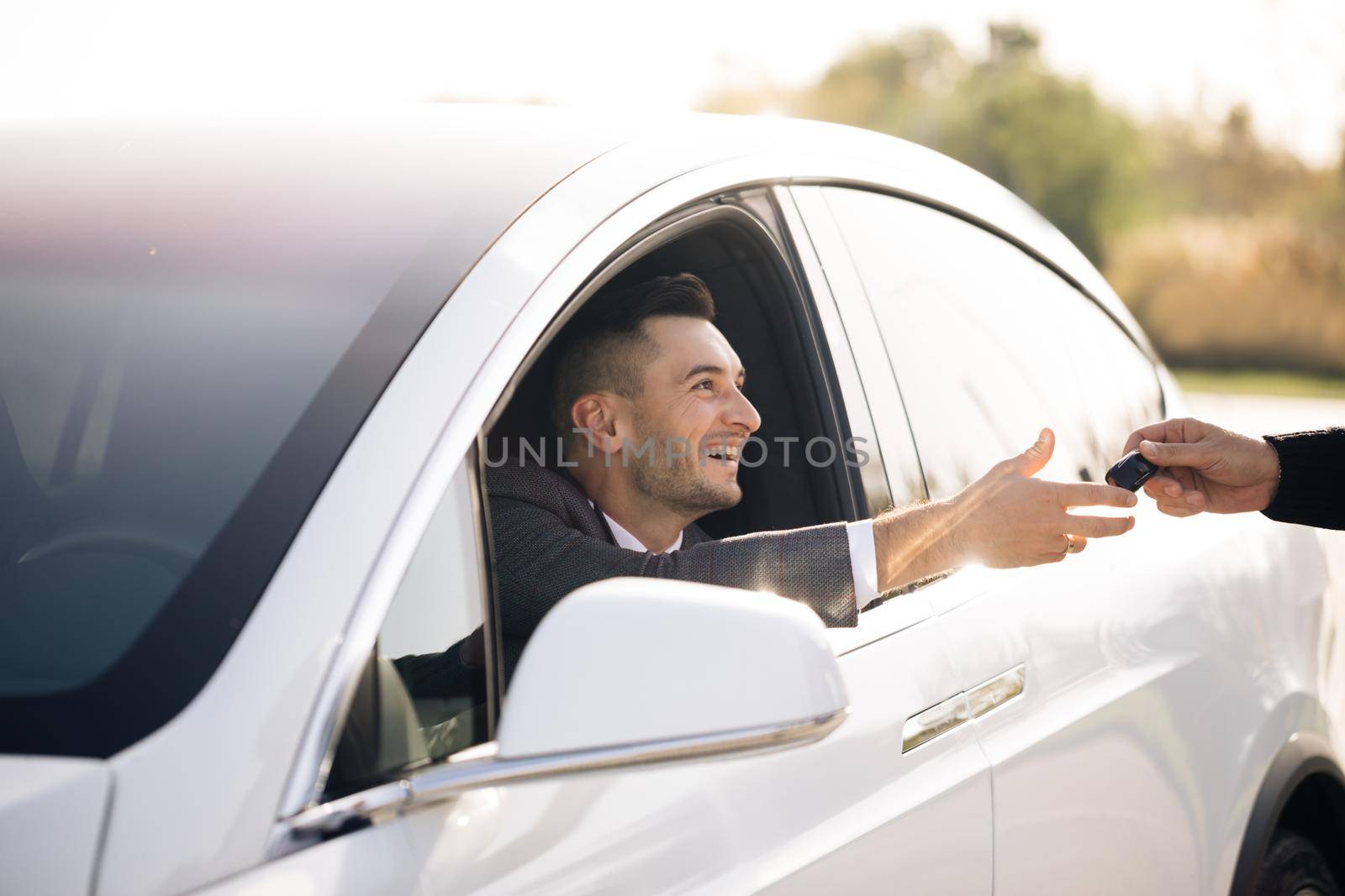 Unrecognized auto seller and a man who bought a vehicle. Dealer giving key to new owner in auto show or salon. Male hand gives a car keys to male hand in the car dealership. by uflypro