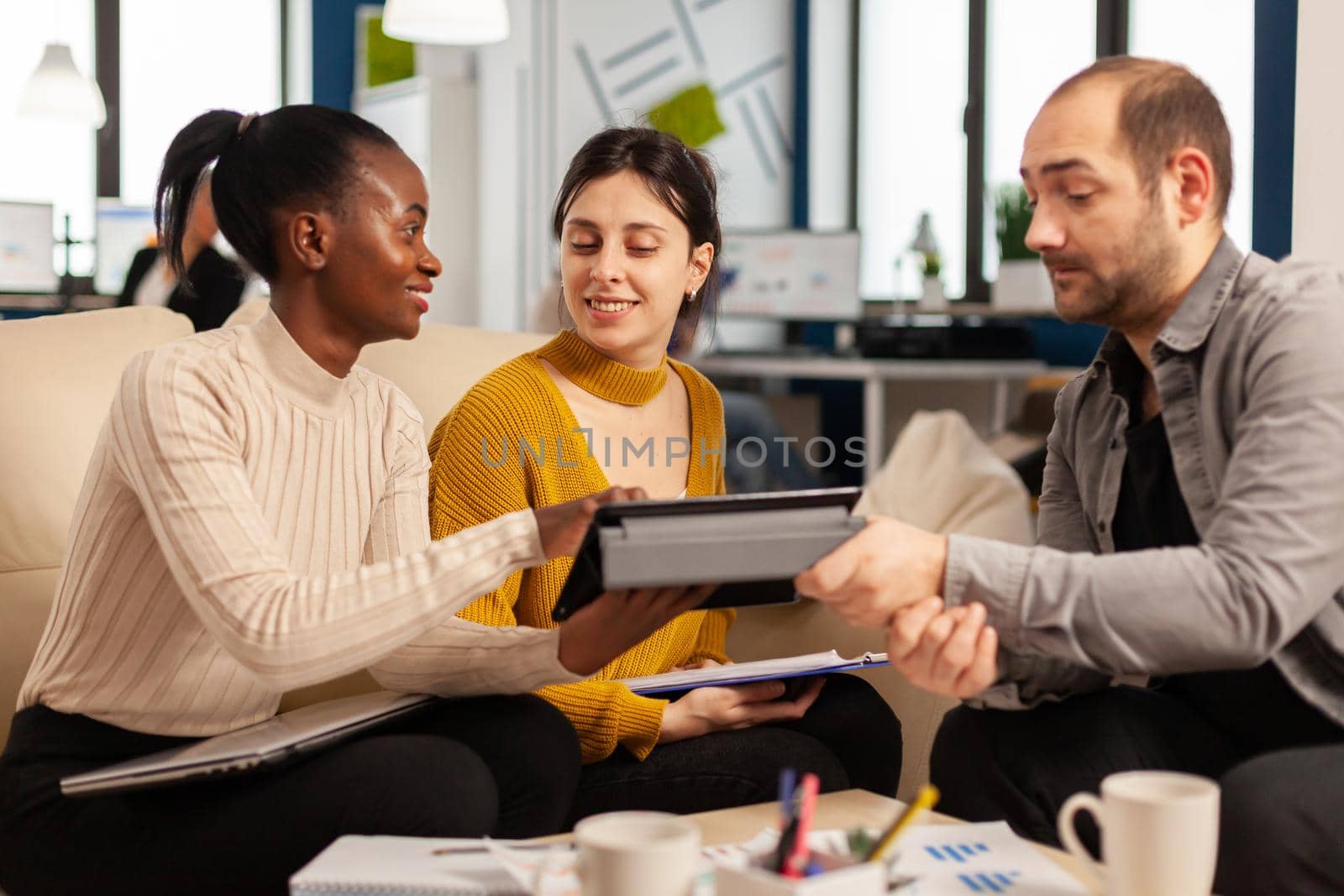 Happy multiethnic group of business people looking at tablet briefing ideas in modern corporate startup company office. Colleagues talking about start up financial team strategy management