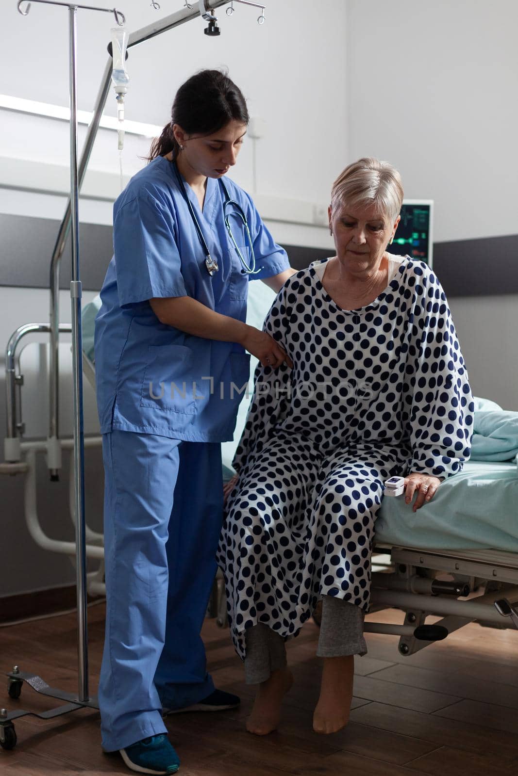 Medical nurse in scrubs helping senior woman in hospital room by DCStudio