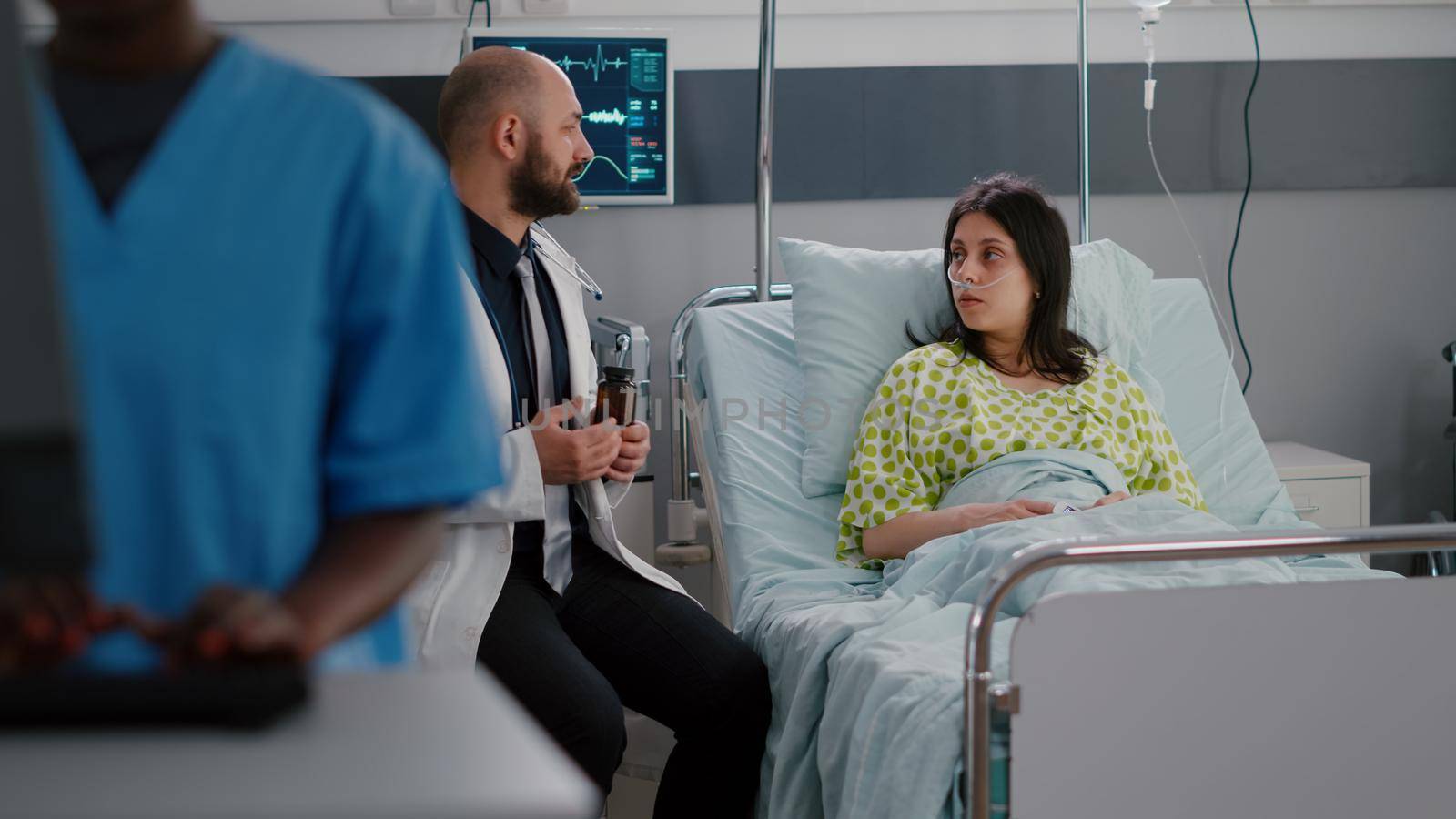 Physician doctor explaining pill medication to sick woman during pharmaceutical appointment in hospital ward. Patient sitting in bed discusssing vitamin prescription consulting healthcare treatment