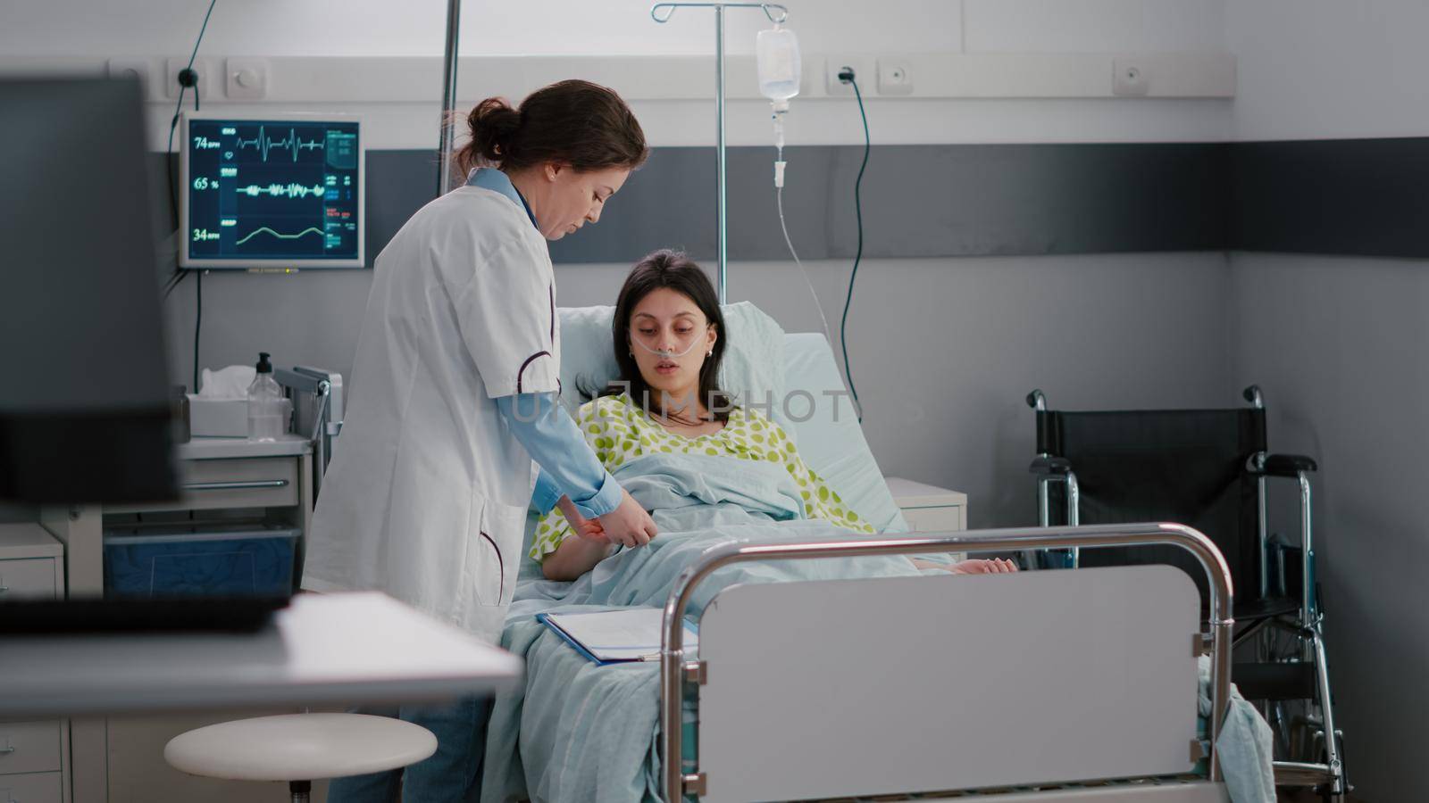 Practitioner specialist checking hospitalized sick woman resting in bed during illness appointment in hospital ward. Doctor putting medical oximeter monitoring pulse measure