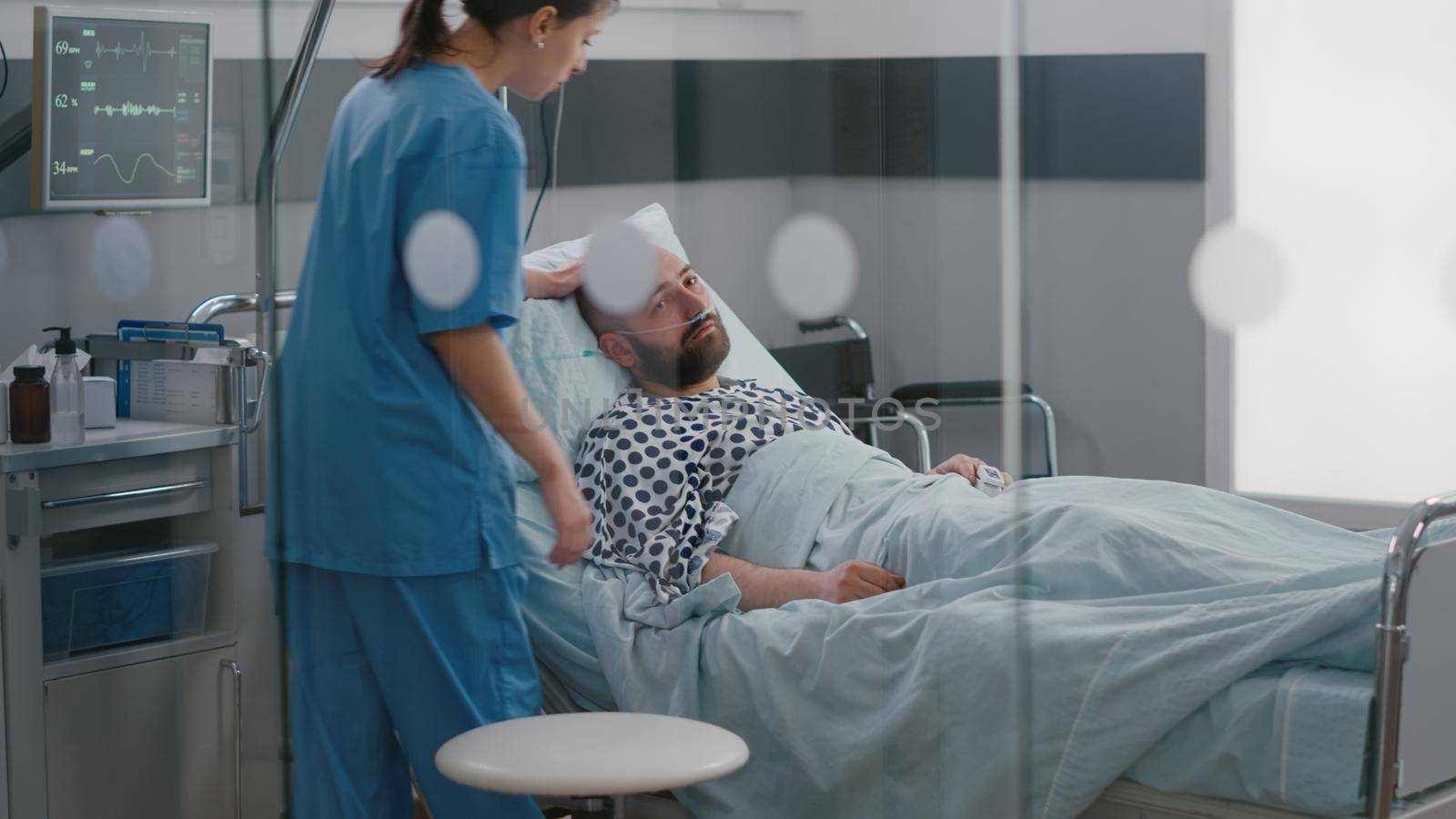 Sick man resting in bed wearing nasal oygen tube waiting practitioner doctor for disease examination after medical surgery in hospital ward. Hospitalized patient having respiratory disorder