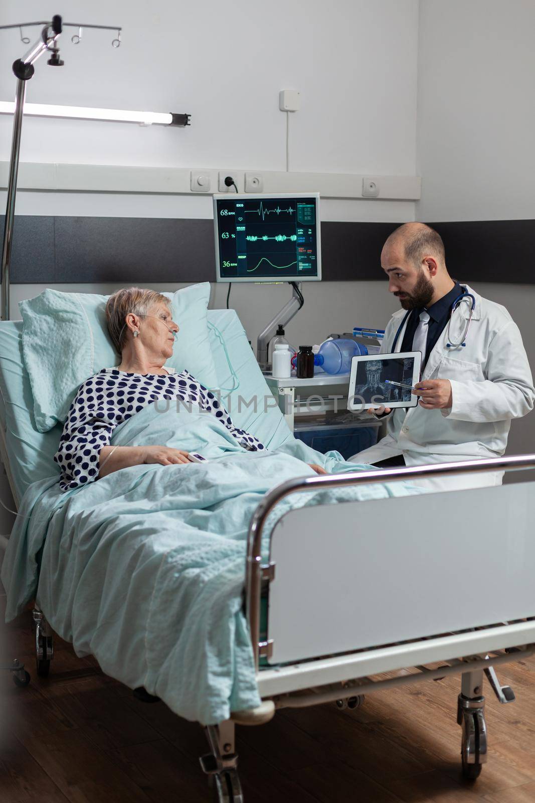 Doctor sitting next to senior man explaining body trauma diagnosis by DCStudio