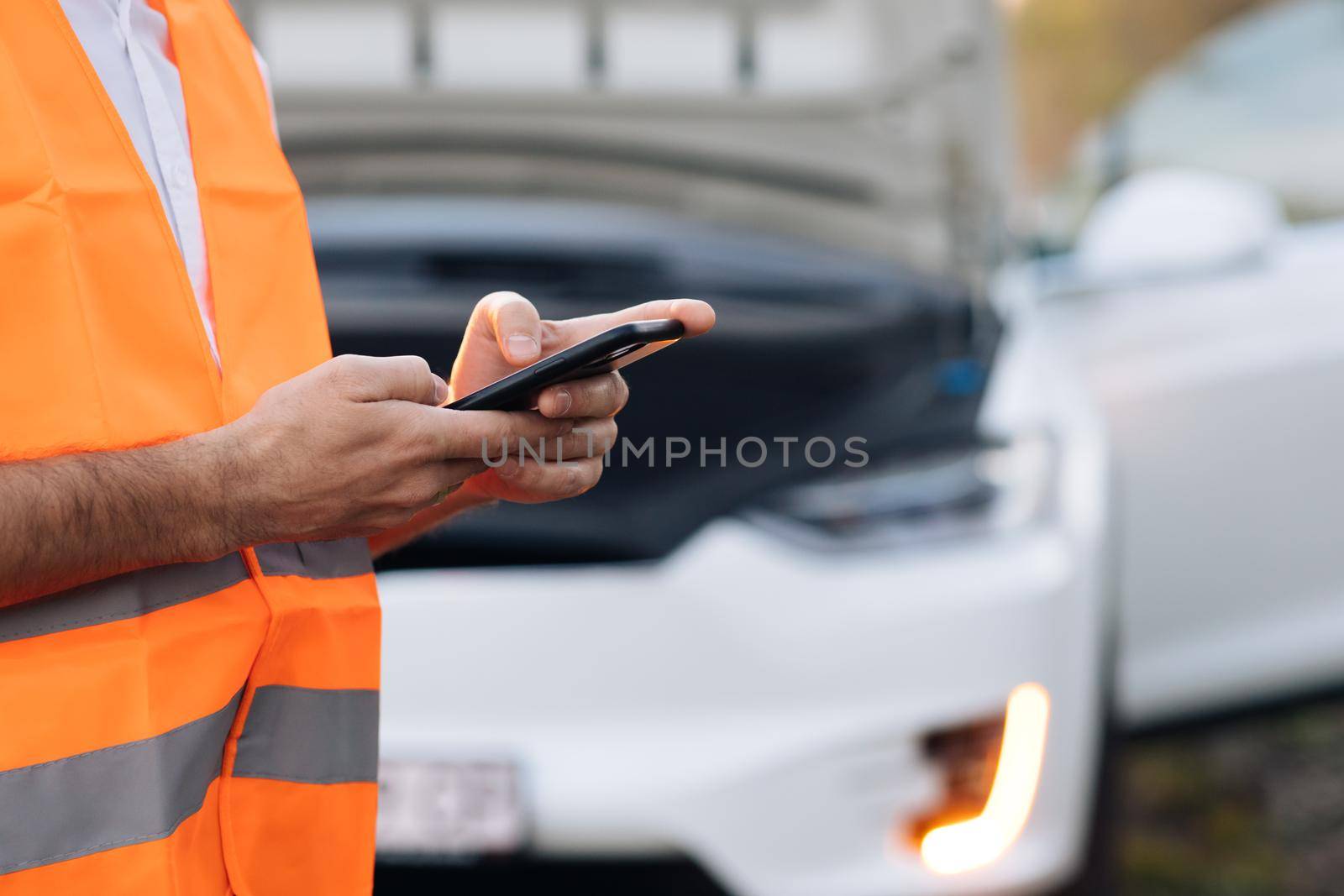 The man uses the phone after the electric car has broken down. Car Blinker Light or Emergency Light. The electric car had an accident. Car service.