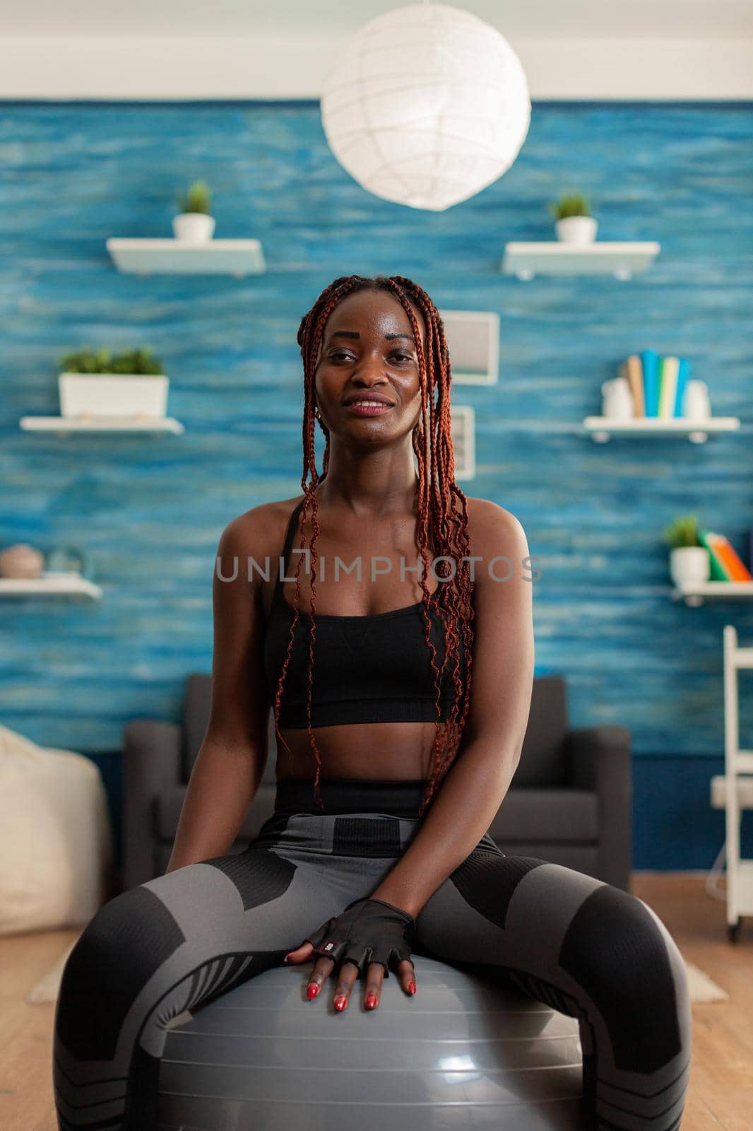 Happy joyful smiling african woman relaxing on swiss ball, after intense hard sport workout on yoga mat in home living room. Cheerful strong athletic fit african using stability ball.