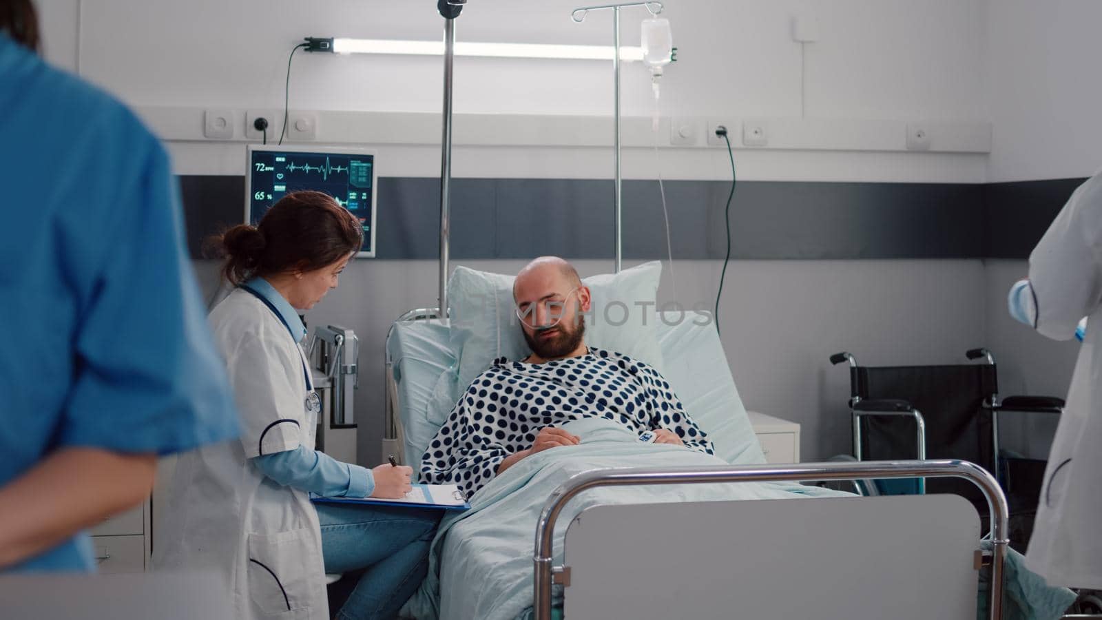 Medical practitioner doctors examining sick man checking sickness symptom during recovery appointment in hospital ward. Patient resting in bed while doctor monitoring pulse