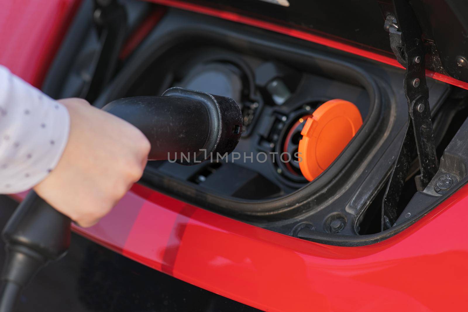 Woman Plugs in Charger into Socket of Her Modern New Red Electric Car. Woman is plugging electric vehicle for charging car battery at parking.