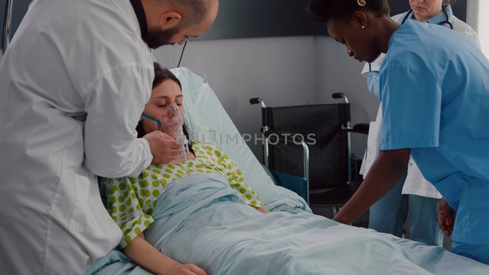 Clinical team monitoring sick woman putting oxigen mask analyzing respiratory sickness during coronavirus pandemic in hospital ward. Black nurse checking heart puls using medical oximeter