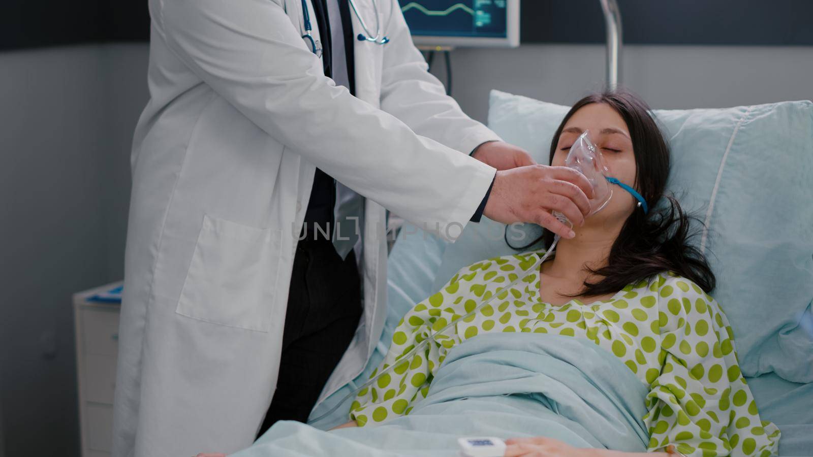 Clinical team monitoring patient putting oxigen mask analyzing respiratory condition during respiratory emergency in hospital ward. Black nurse checking heart puls using medical oximeter