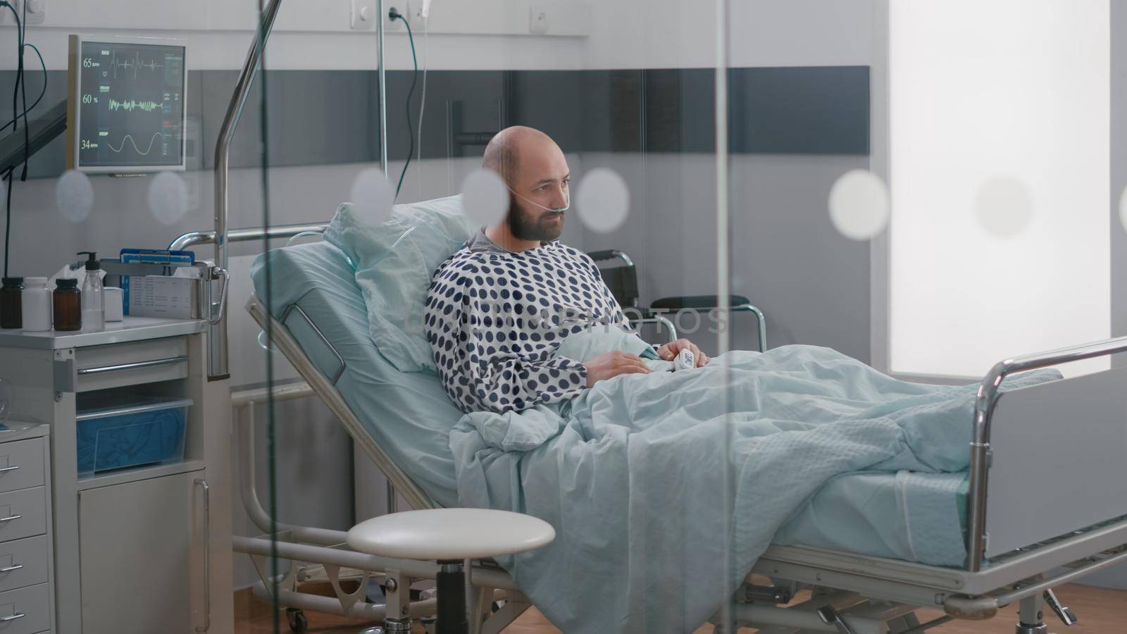 Stressed sick man sitting in bed waiting for respiratory treatment recovering after sickness surgery in hospital ward. Hospitalized patient looking into camera wearing nasal oxygen tube
