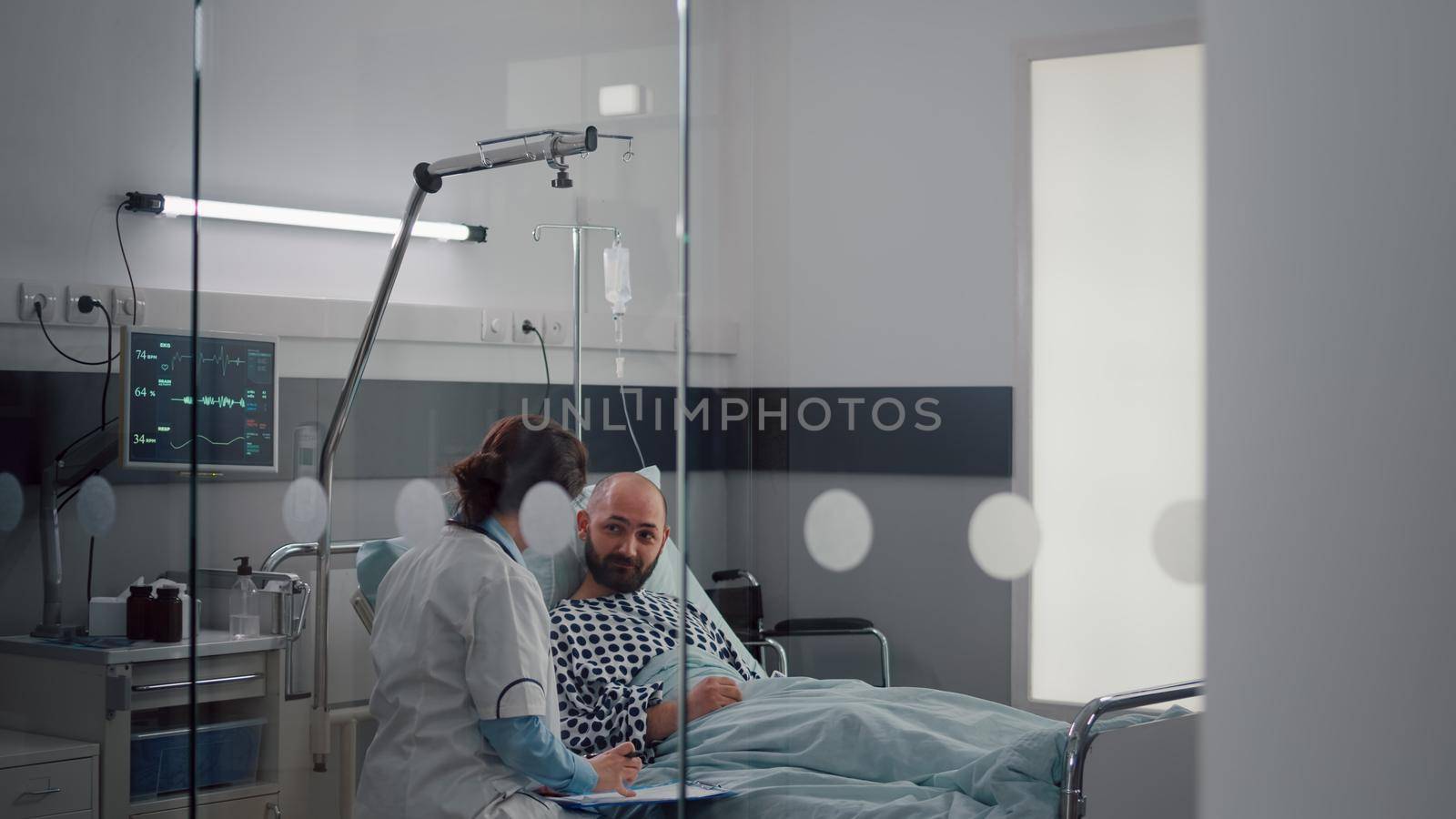 Medical asssistant checking patient vitals monitoring heart rate injecting vitamin in iv fluids drip bag in hospital ward. Doctor physician discussing medical treatment explaining healthcare treatment