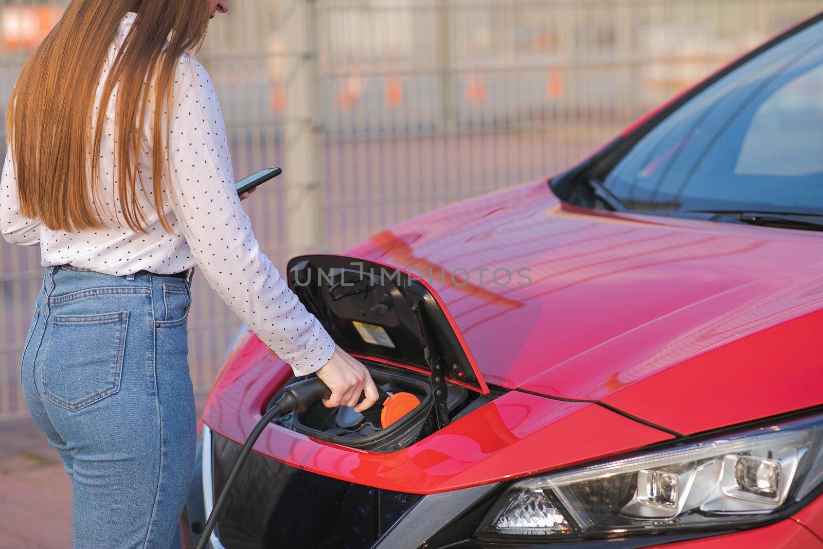 Woman Hand Attaching Power Cable To Environmentally Friendly Zero Emission Electric Car. Woman makes power supply plugged into an electric car being charged