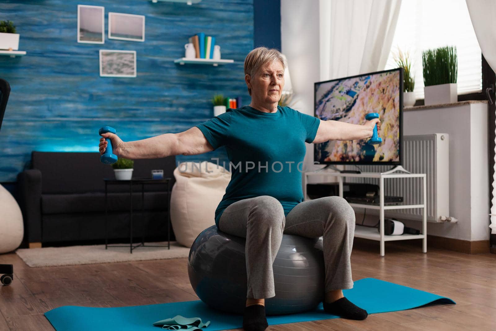 Focused senior woman stretching arm working at body muscle using fitness dumbbells by DCStudio