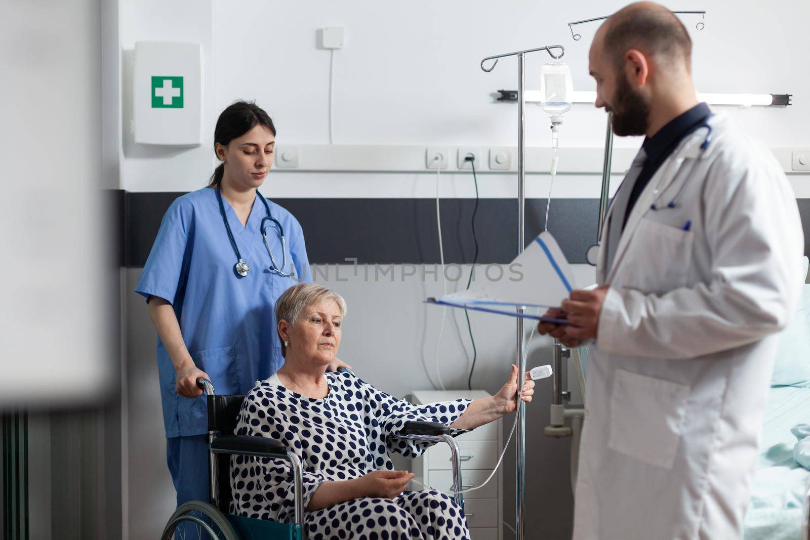 Elderly sick patient sitting in hospital wheelchair getting treatment by DCStudio