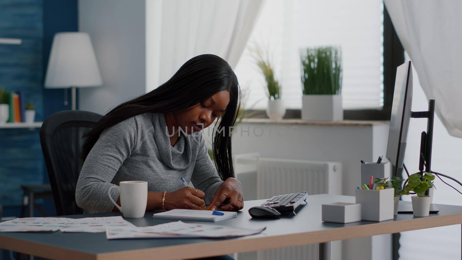 Black student writing education ideas on stickey notes sitting at desk table in living room. Young woman studying business at univeristy using elearning platoform working remote from home