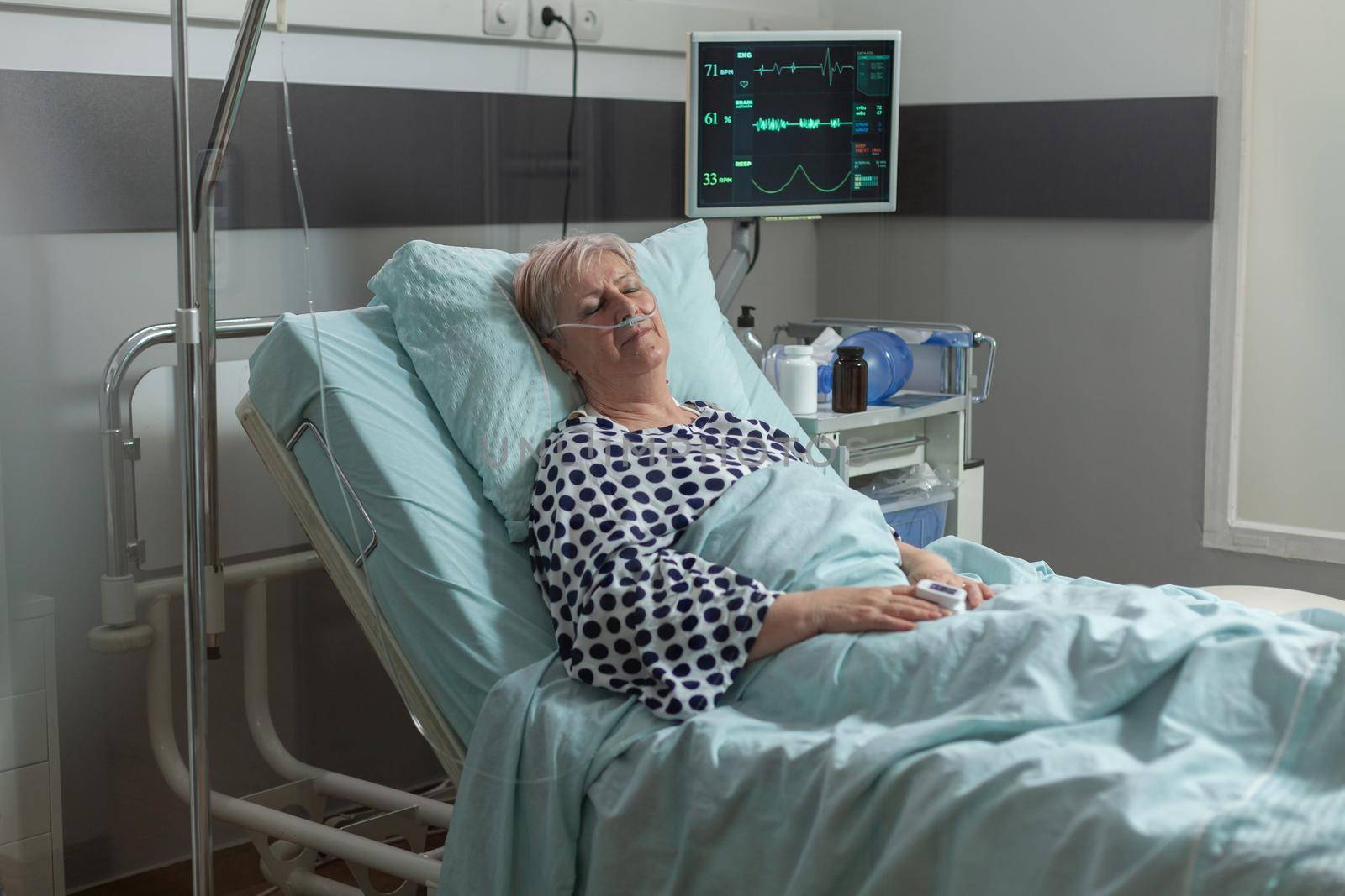 Senior woman resting in hospital bed breathing with help from oxygen mask by DCStudio