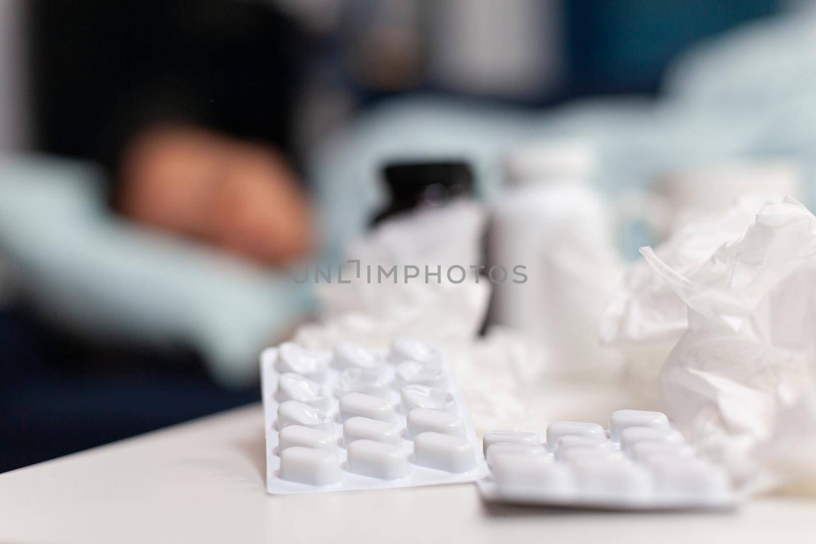 Close up of pills and napkins for ill sick woman resting on the sofa at home. Taking medicine for cold and flu, fever, seasonal virus symptoms. Bottles with drugs for recovery treatment