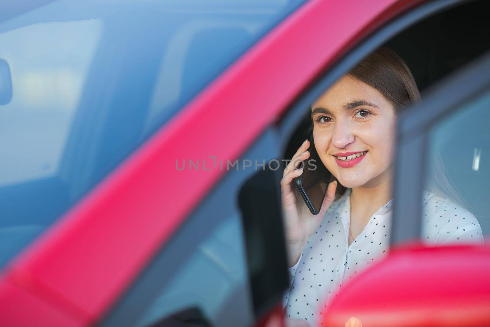 Girl using smart phone and waiting power supply connect to electric vehicles for charging the battery in car. Positive young girl talking on the phone sits in electric car and charging